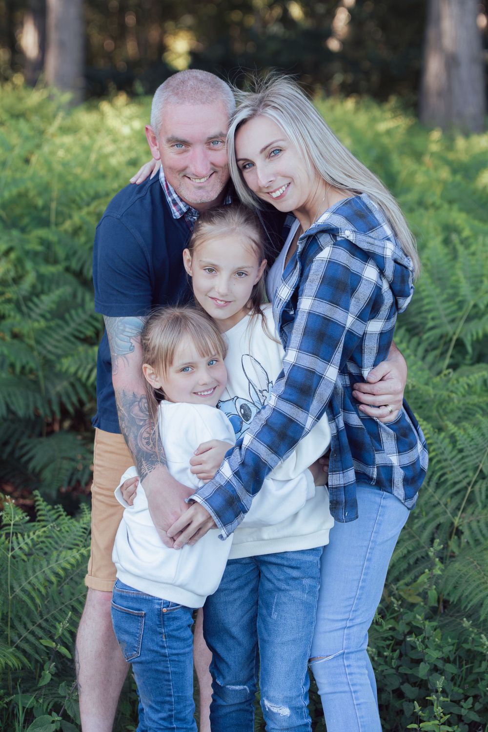 Family portrait of four people embracing outdoors in a forest setting.