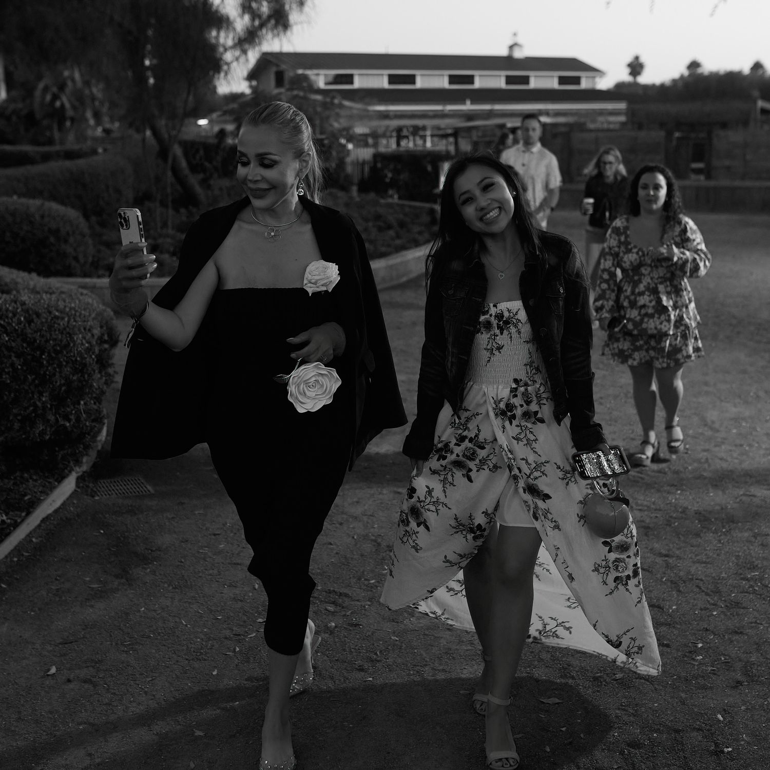 Black and white photo of friends walking together outdoors wearing casual and floral dresses.