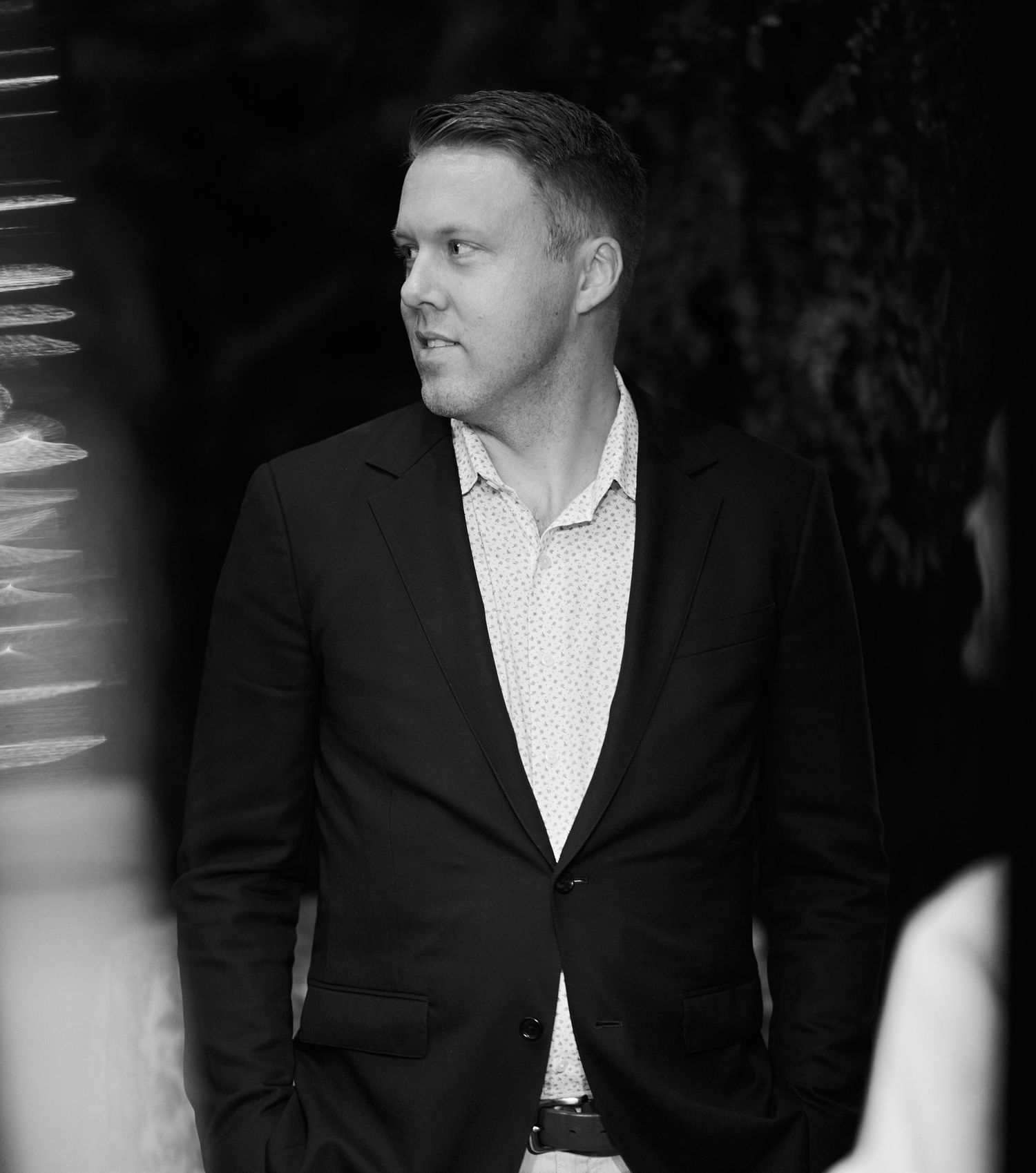 Professional black and white portrait of a man in a suit jacket looking thoughtfully to the side.