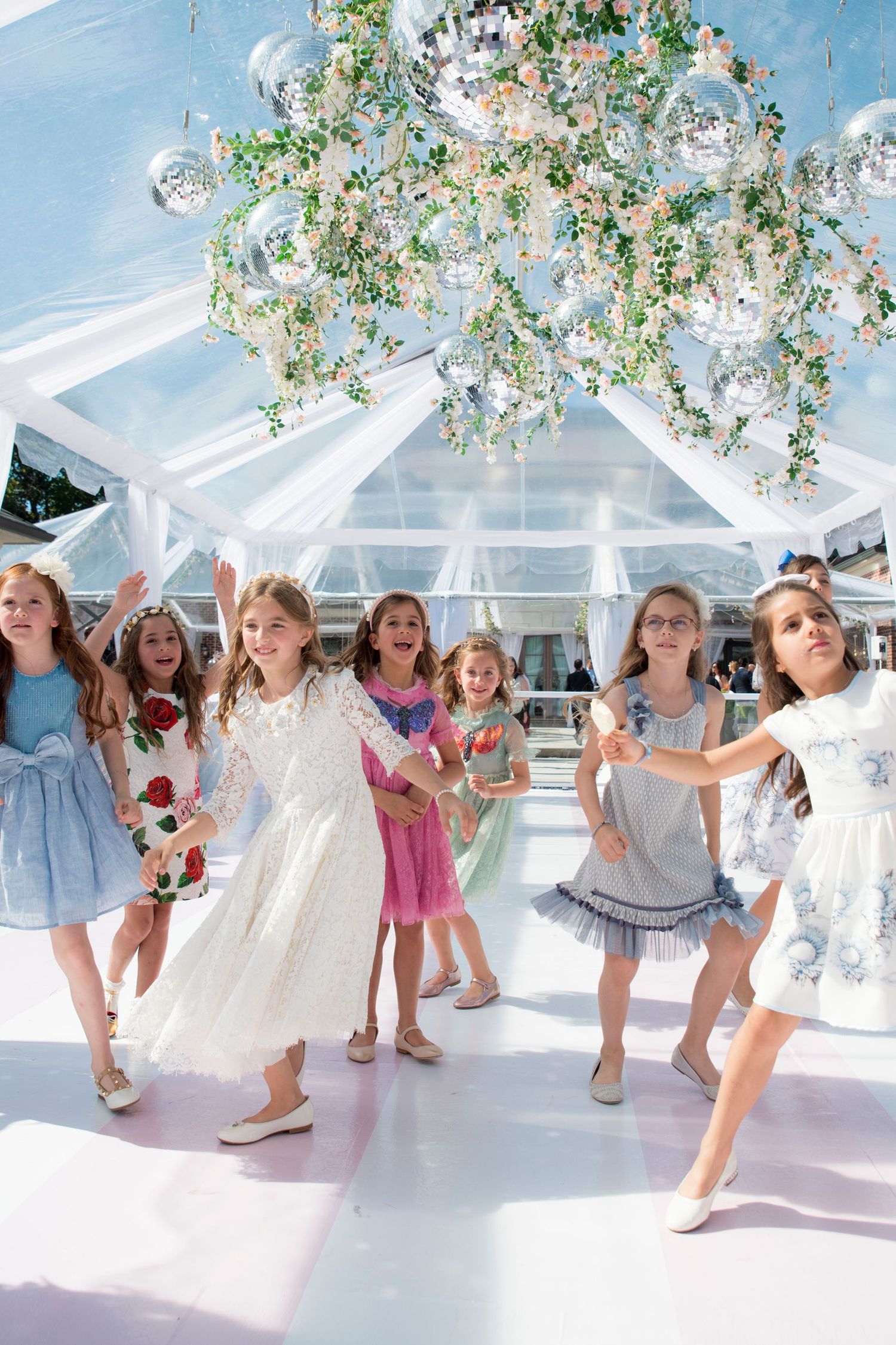 Children dancing in a white gazebo decorated with floral arrangements and crystal balls.