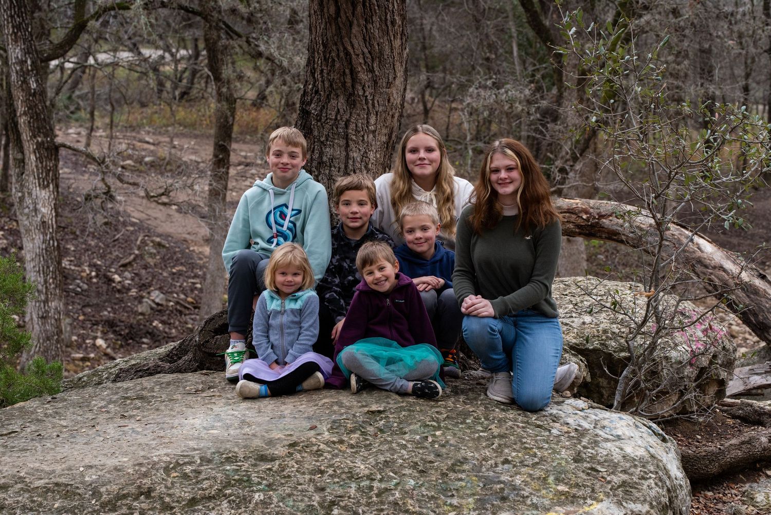 A casual outdoor family portrait taken on a large rock in a wooded setting.