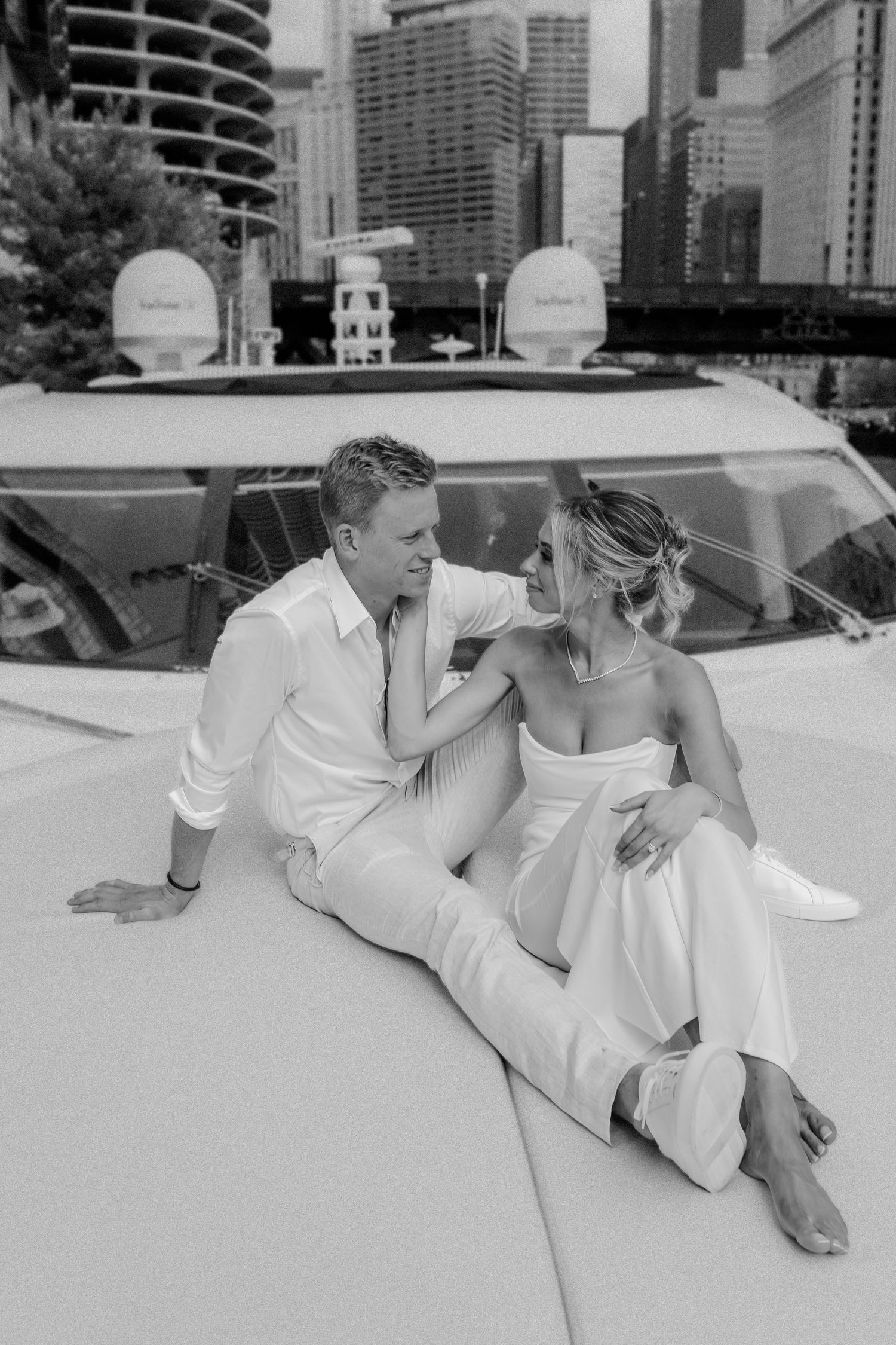 A couple in white outfits sit intimately together on a boat with the Chicago skyline visible in the background.
