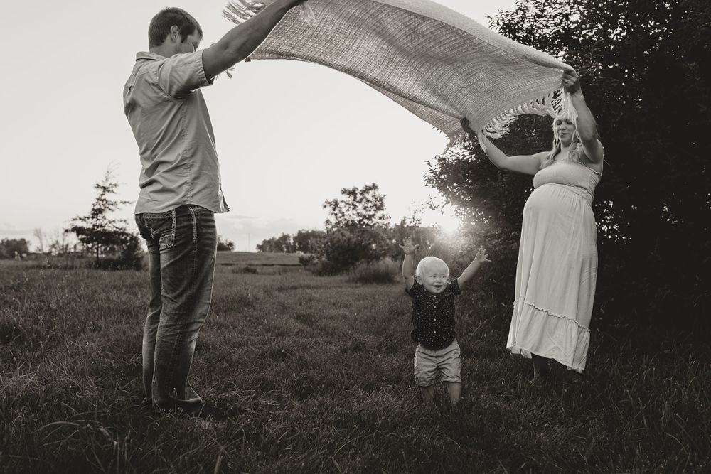 Family plays with blanket in field during sunset creating silhouette effect.