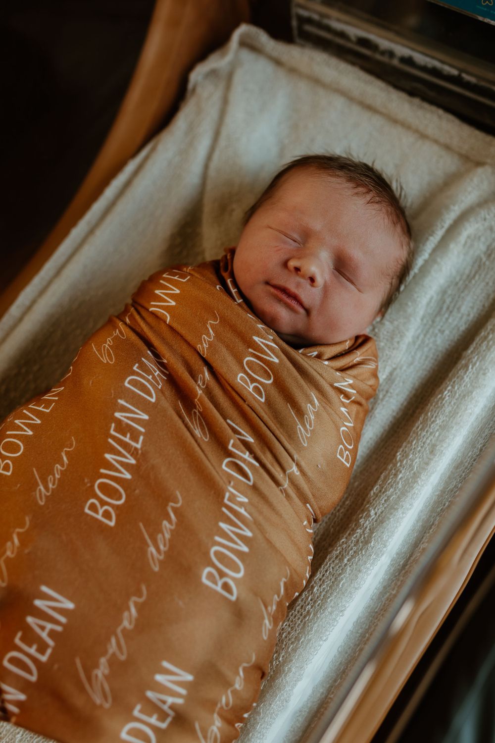 A sleeping newborn swaddled in a brown text-printed blanket.