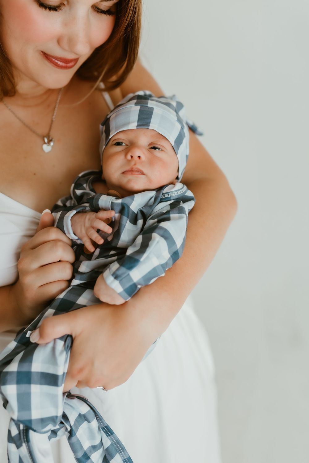 A baby wearing a blue and white plaid outfit is held in loving arms against a white background.