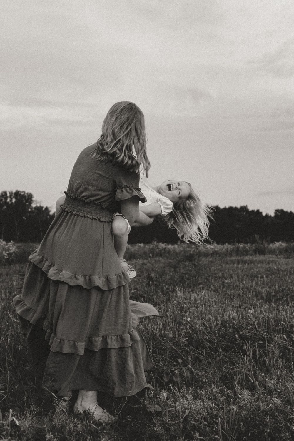 Black and white photo of two people in dresses dancing in a field.
