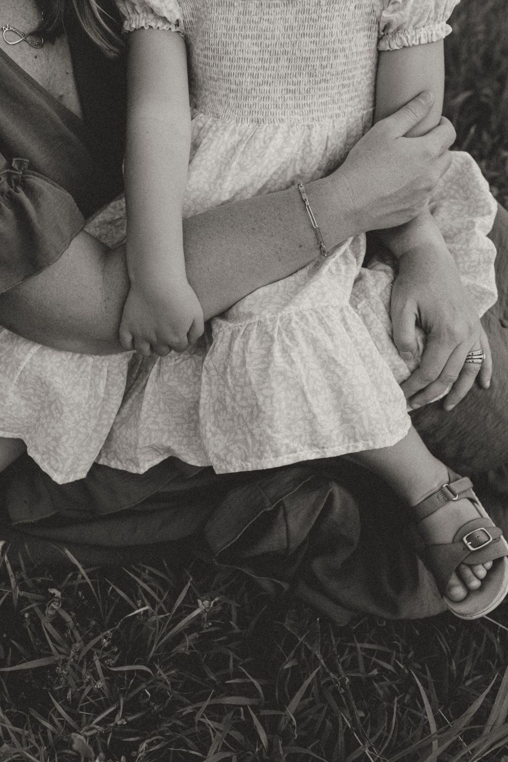 Close-up black and white photo of hands resting on white ruffled dress.
