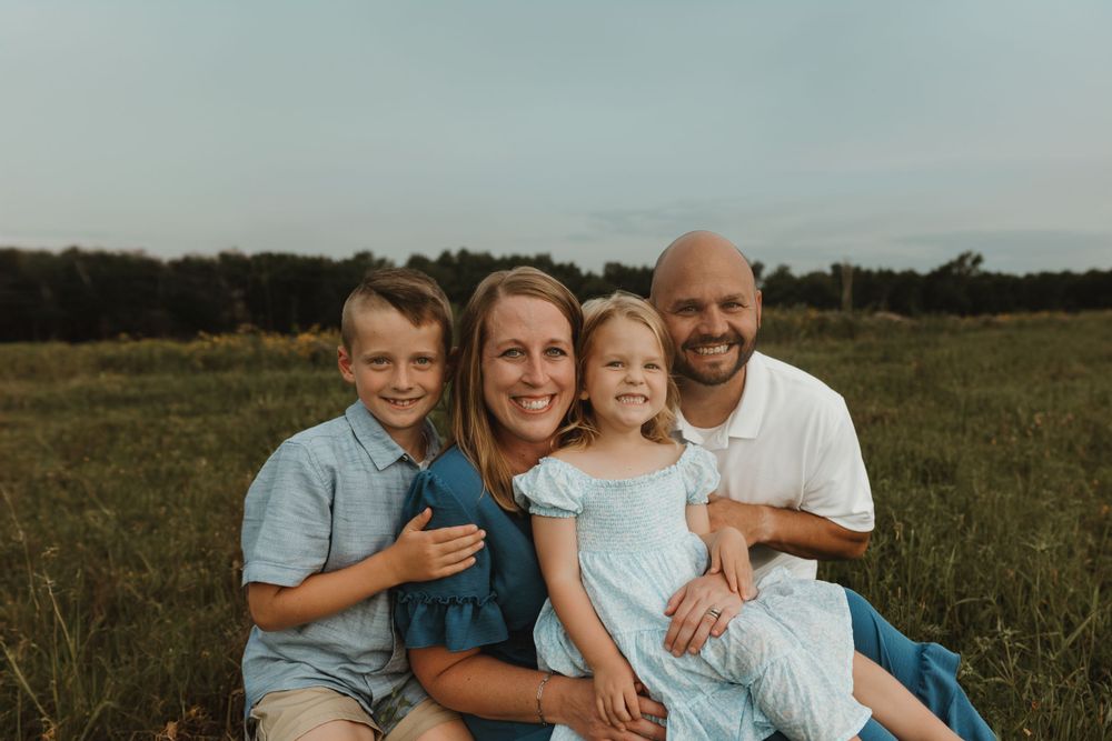 Family of four sitting together in casual attire on grassy field at sunset.