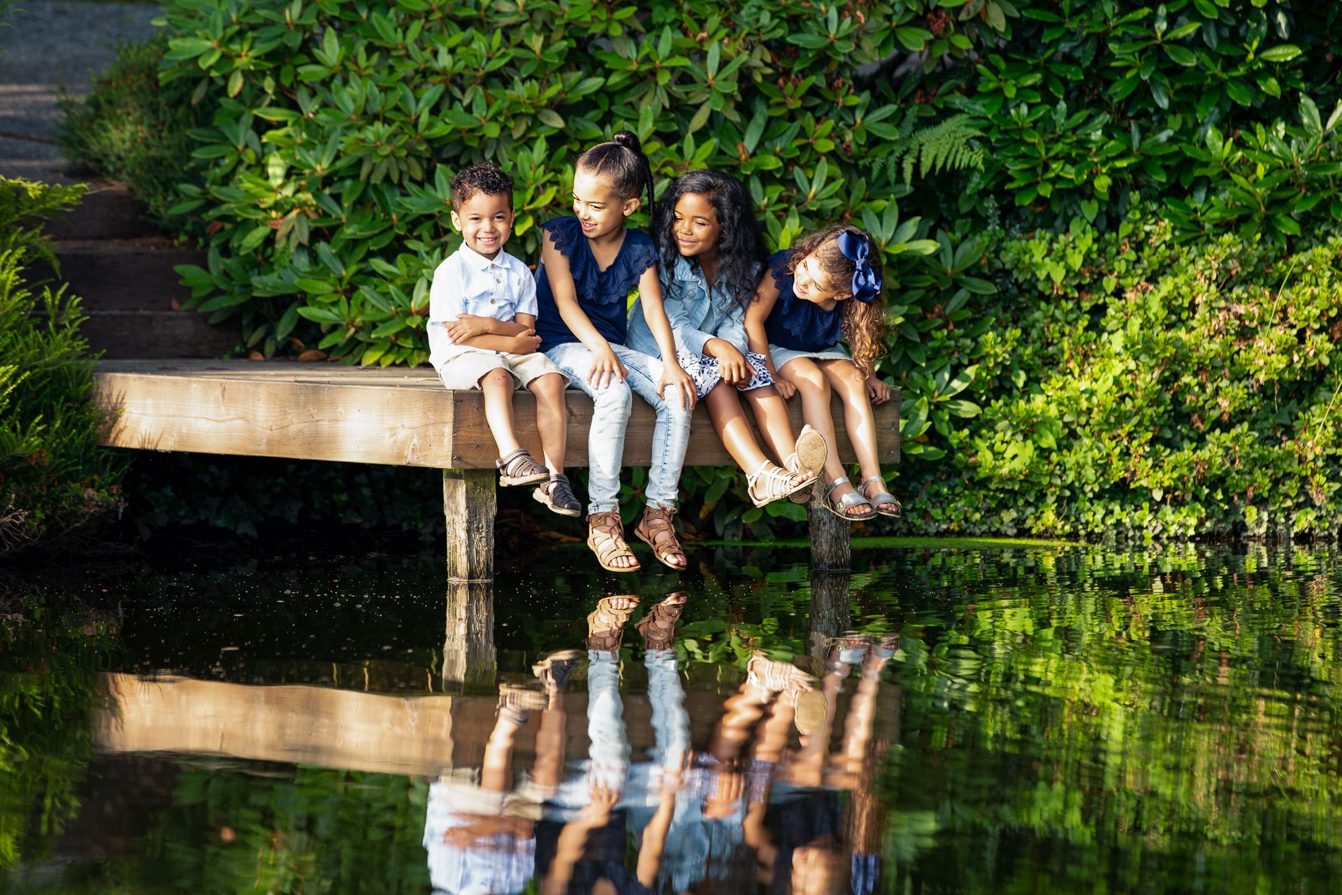 Extended family portrait session by a scenic pond with natural landscaping and stone features.