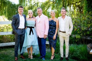 Group photo of wedding guests gathered under weeping willow trees in summer garden.