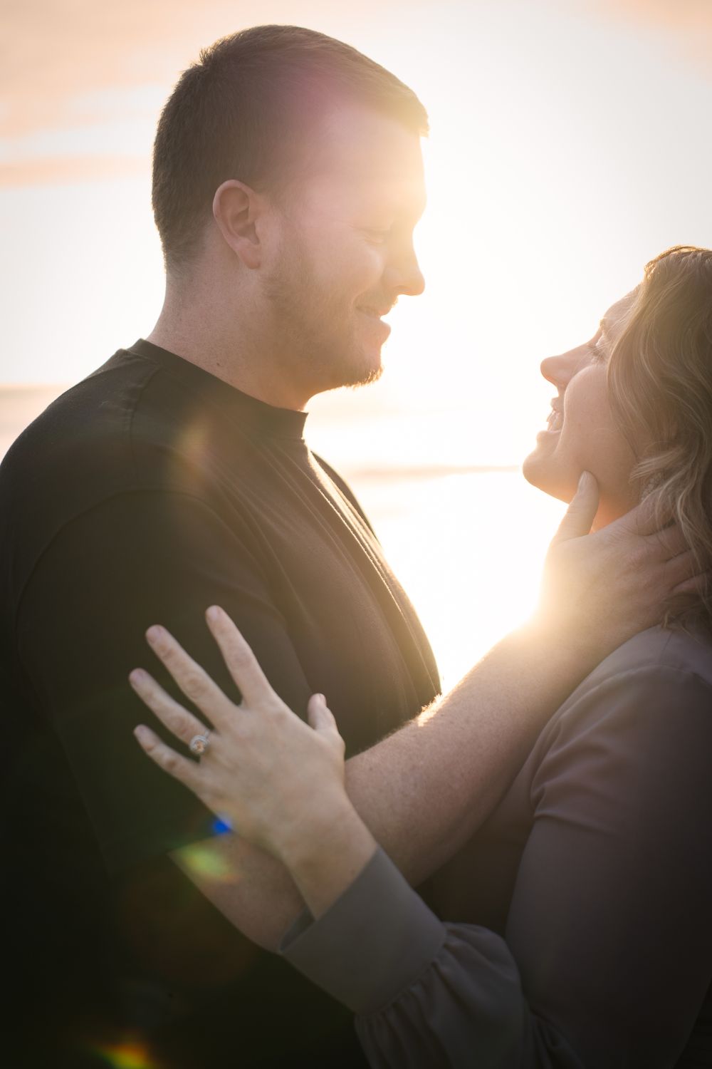 A loving engaged couple embraces in glowing sunset light creating a romantic silhouette against the warm sky.
