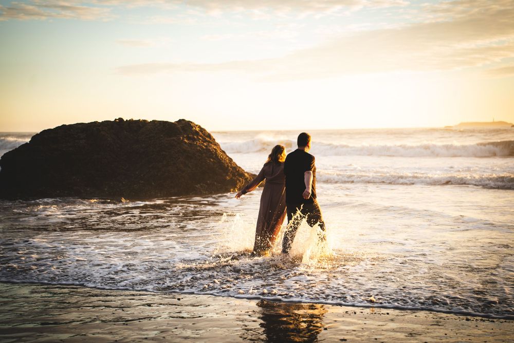 Silhouettes of engaged couple walking together along a Washington beach shoreline at golden sunset.
