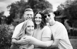 Black and white photo showing a family embracing and smiling together outdoors.