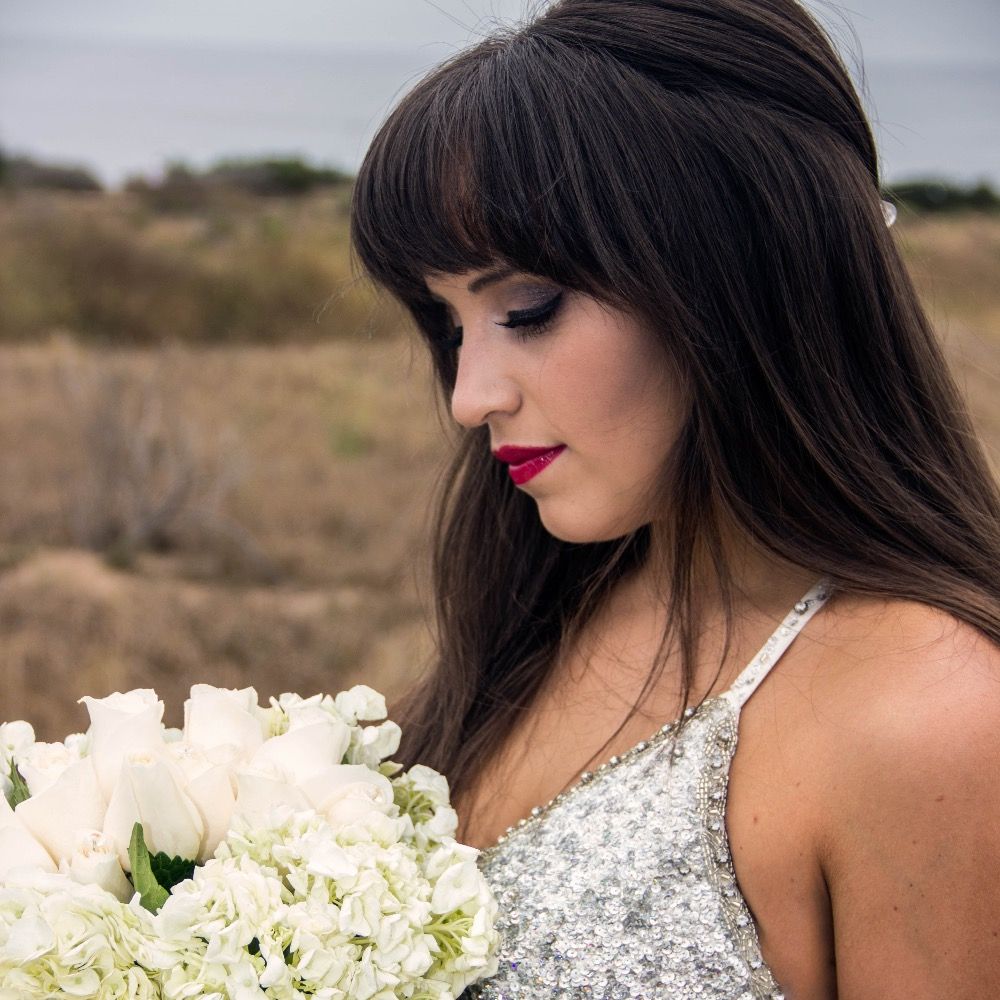 Bride with dark hair and red lipstick holds white bouquet in silver sequined dress.