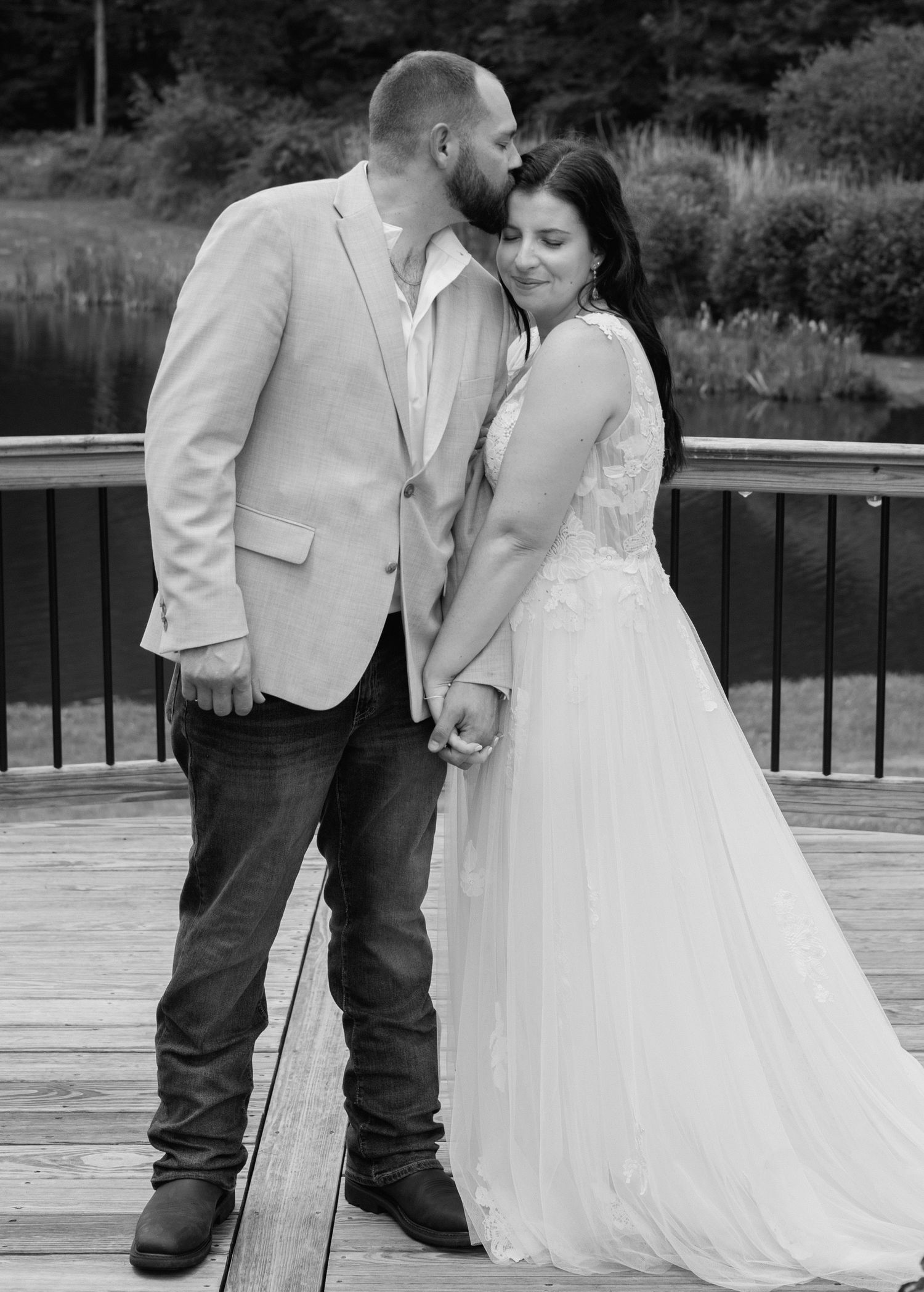 Romantic couple in wedding attire share an intimate moment on a wooden deck.