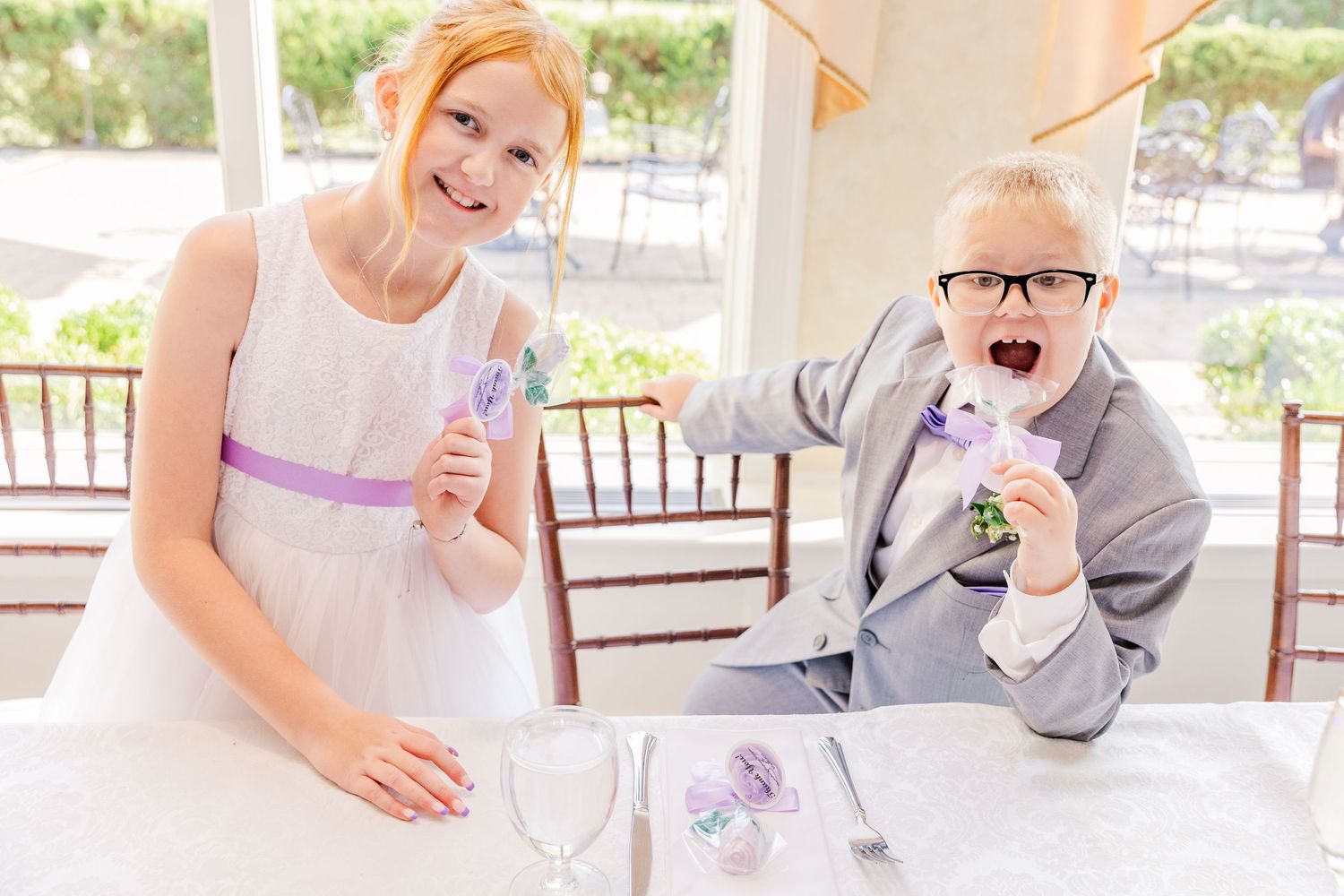 Two children enjoying treats at an elegantly set table with purple accents.