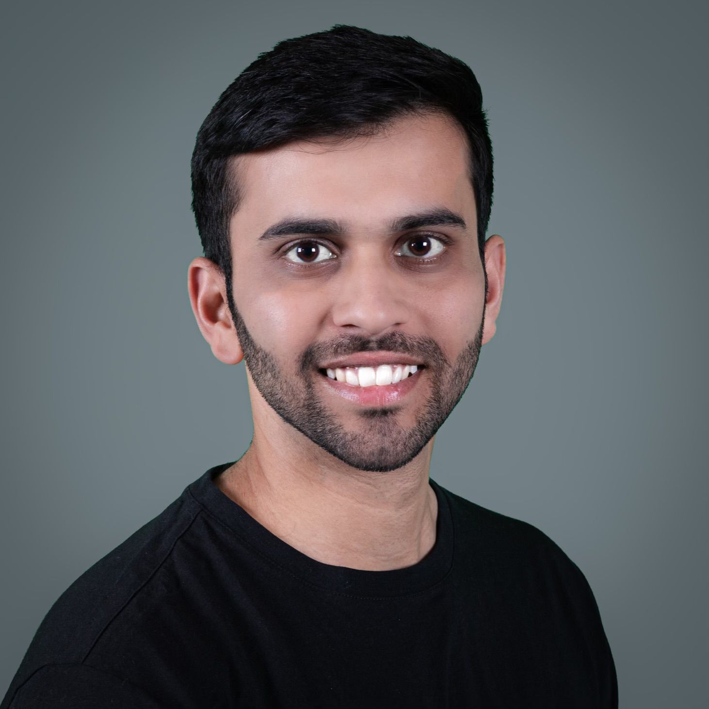 Professional headshot of a person in a black shirt smiling against a grey background.