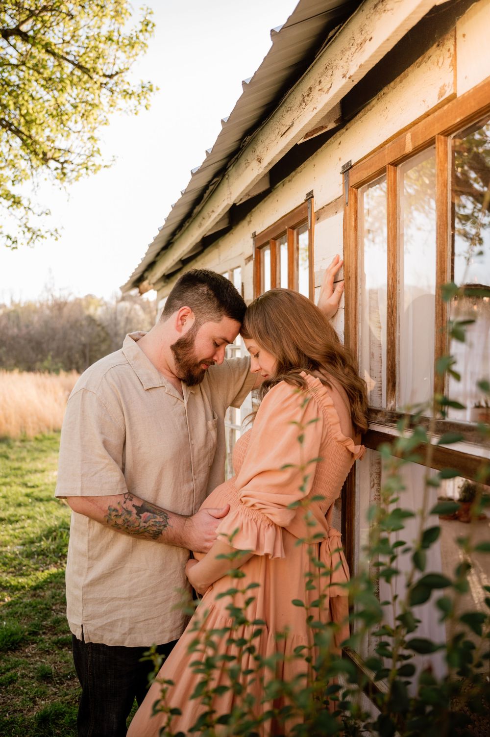 A couple shares a tender moment leaning together against a rustic building at golden hour.