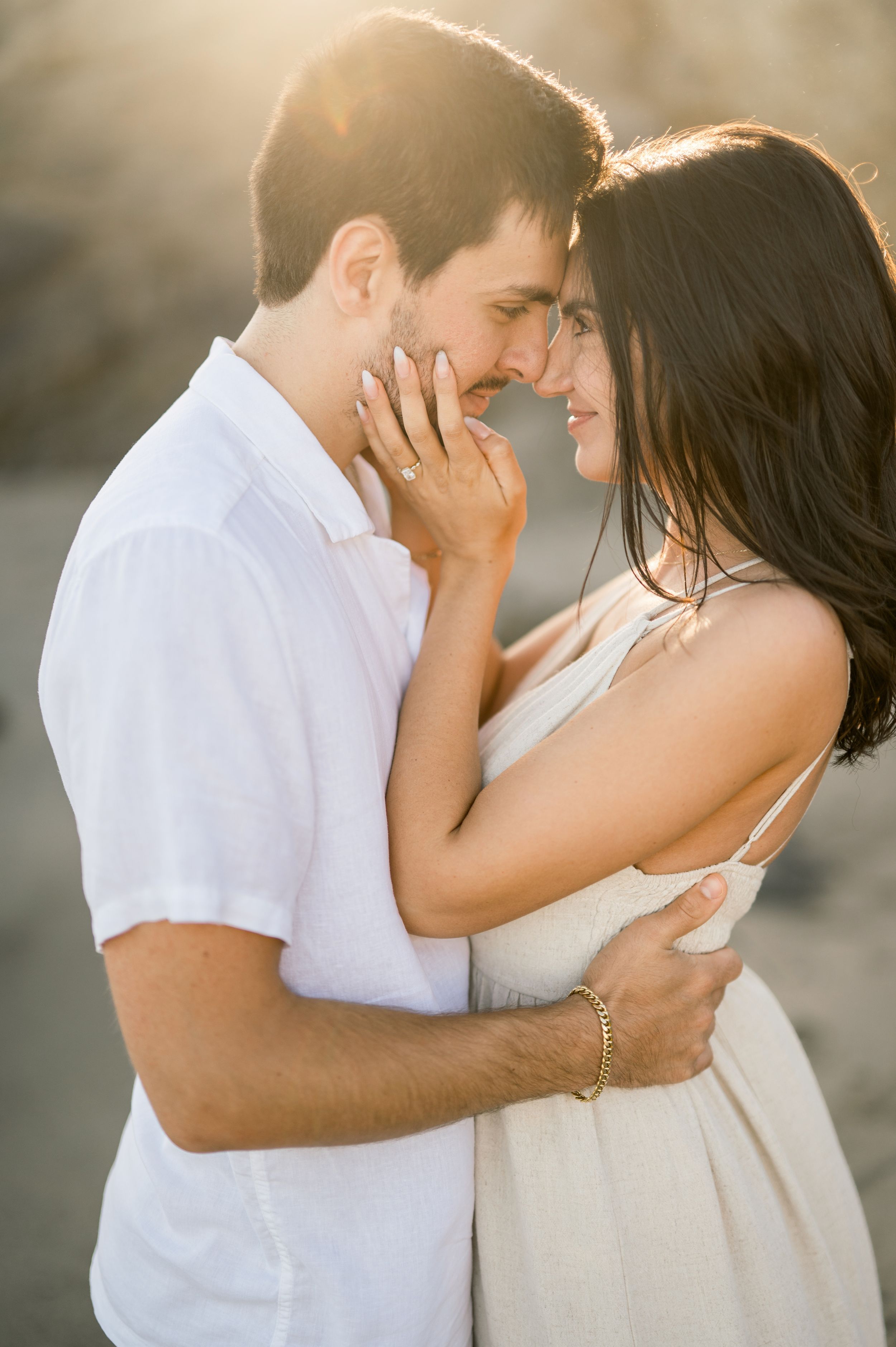 An intimate moment between a couple in white outfits embracing during a sunset beach photoshoot.