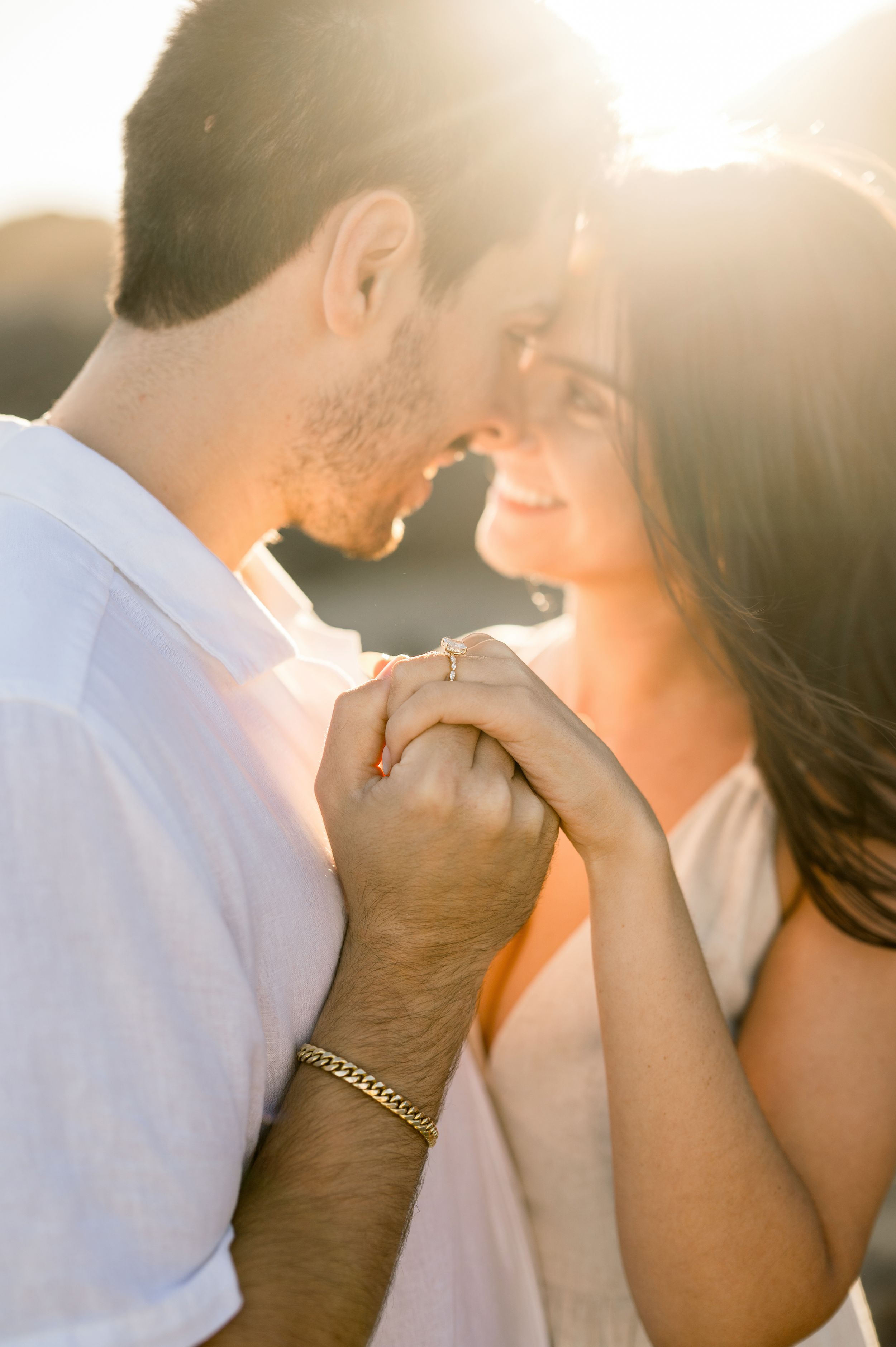 A couple holding hands and sharing an intimate moment in warm sunset lighting at the beach.