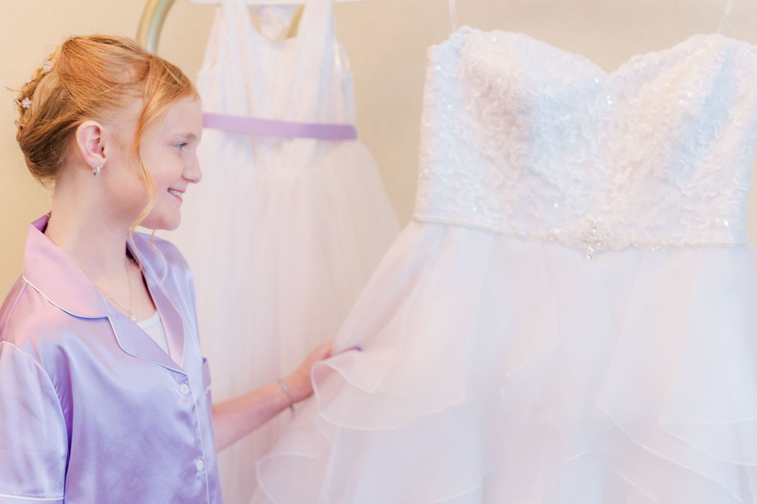 Person in pink robe examining details of white wedding dress.