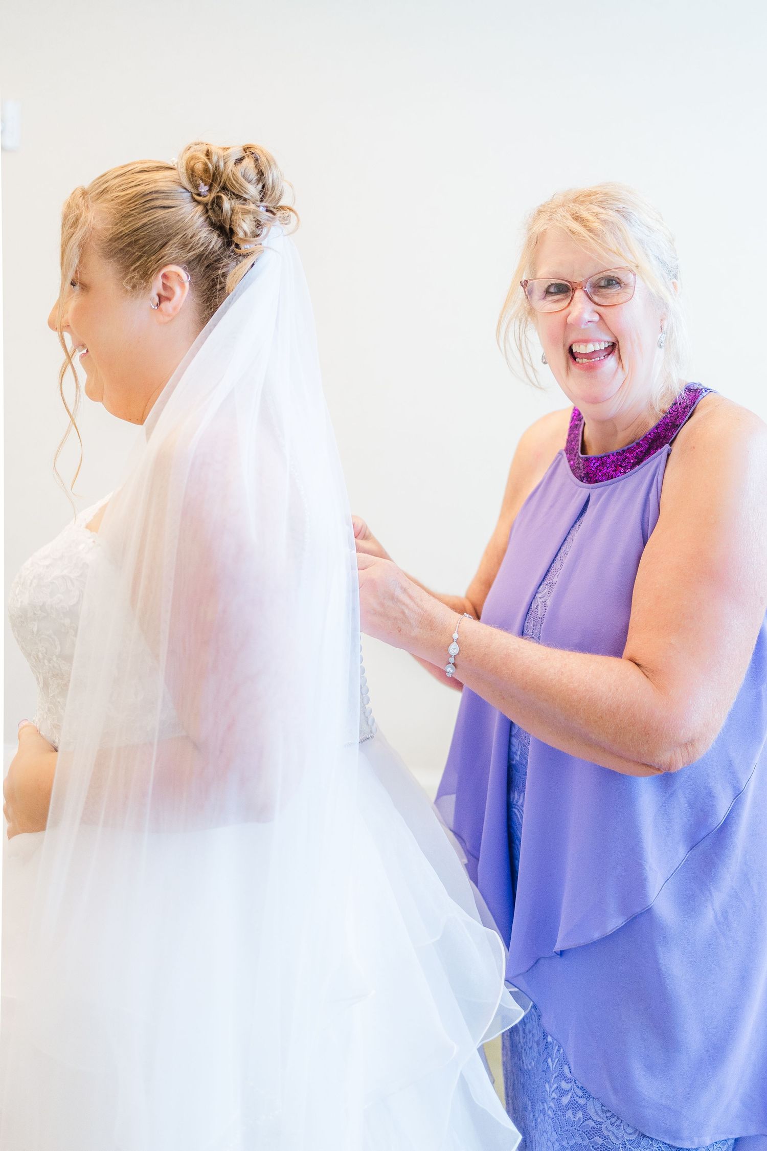 A bride in a white wedding dress getting help with her veil from someone wearing a purple dress.