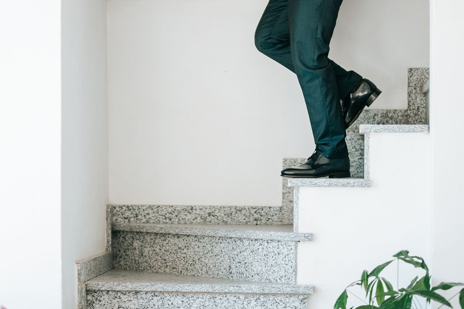 Man in dress pants and black shoes climbing granite stairs in a modern white interior.