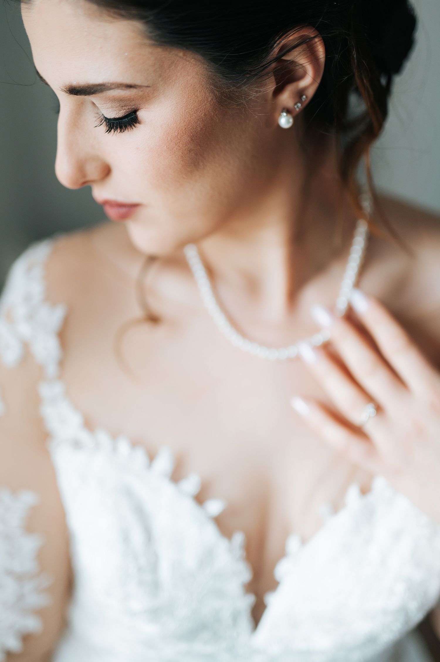 Elegant bride wearing pearl necklace and earrings in lace wedding dress.