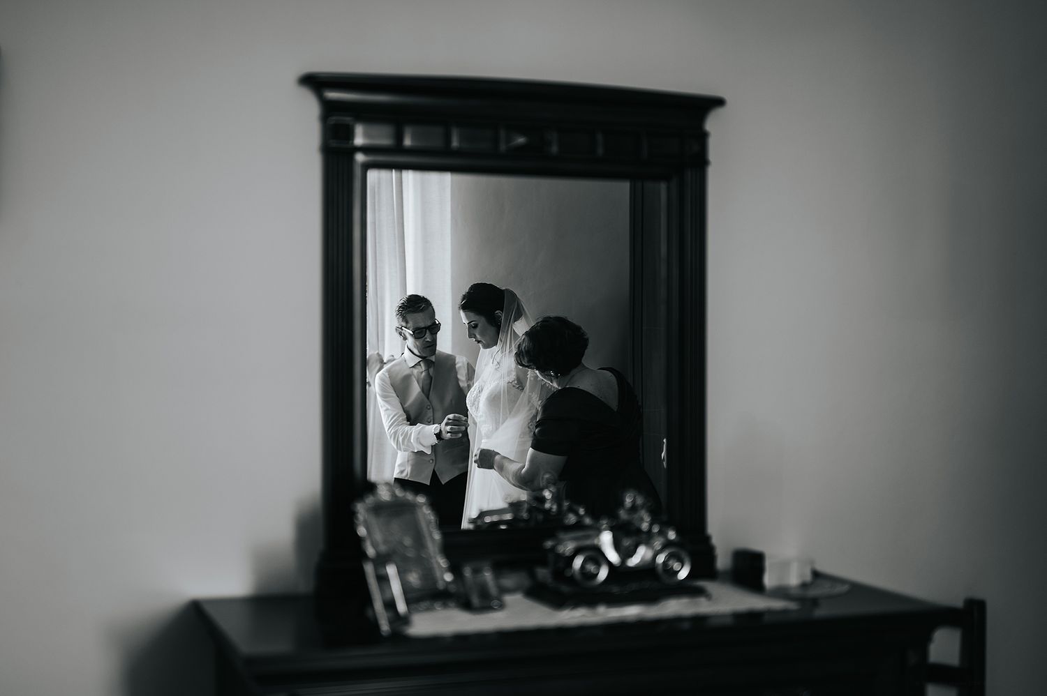 Black and white mirror reflection of bride getting ready with assistant.