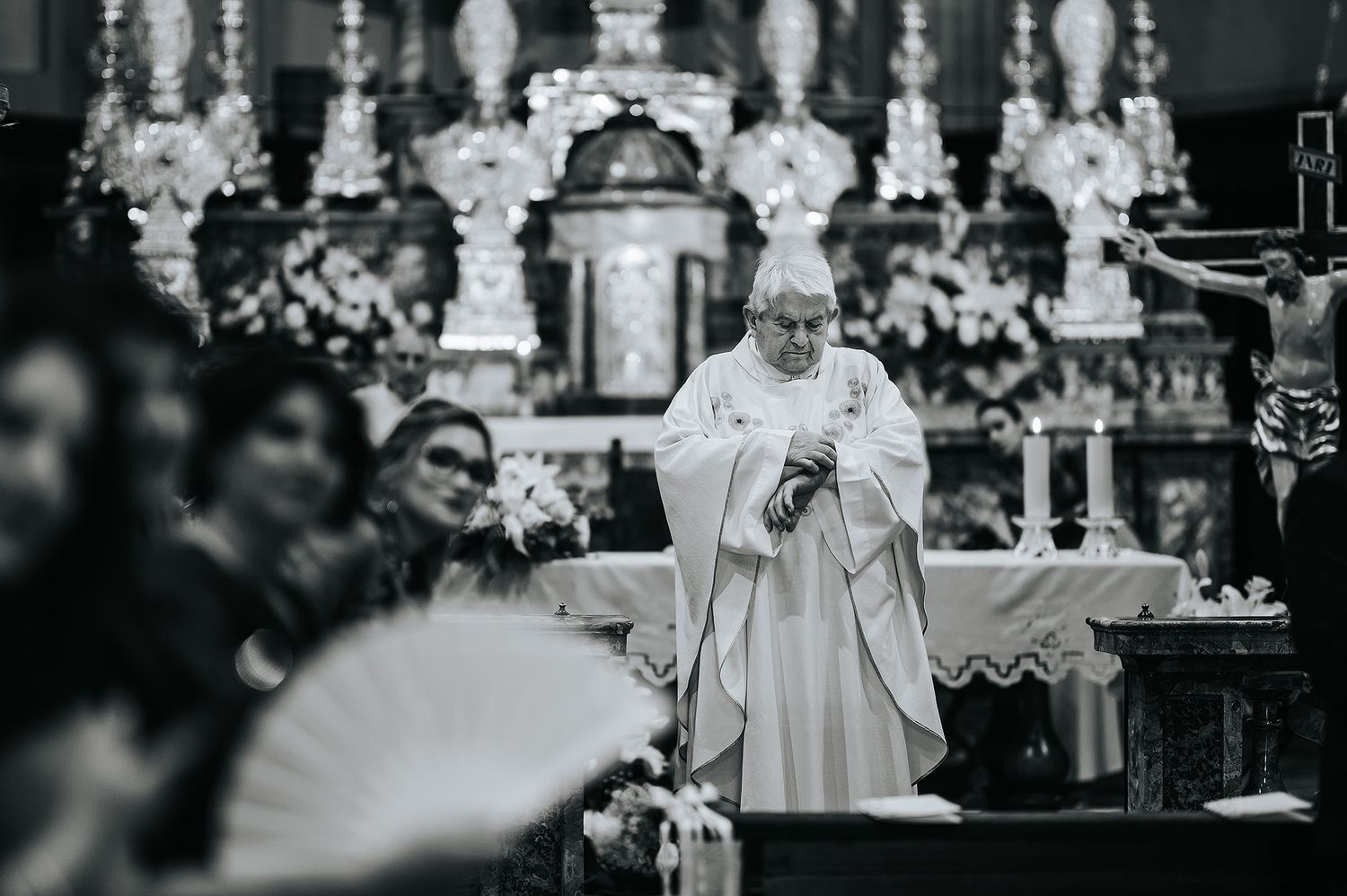 Black and white photo of priest performing wedding ceremony at ornate church altar with floral decorations.