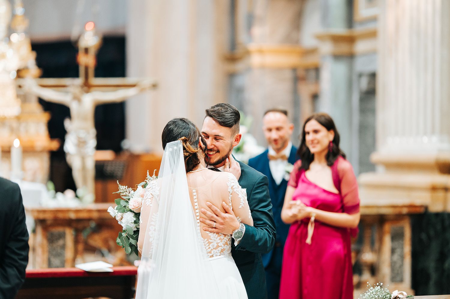 Groom embracing bride at church altar during wedding ceremony, with guests watching in background.