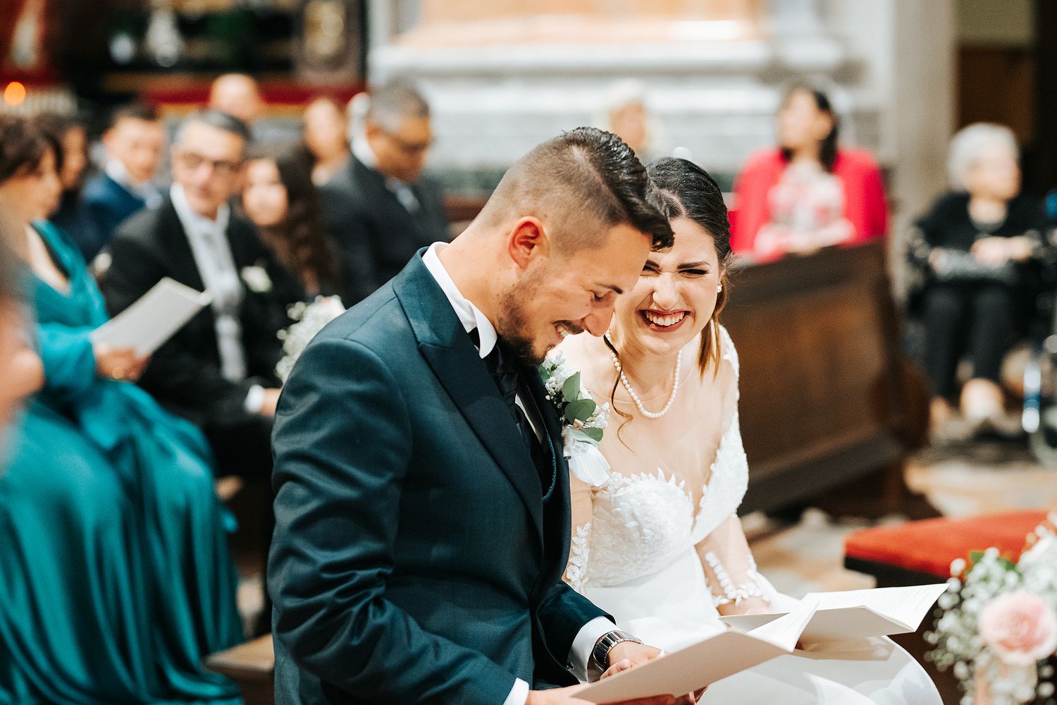Bride and groom laughing together while seated during wedding ceremony in a grand historic church.
