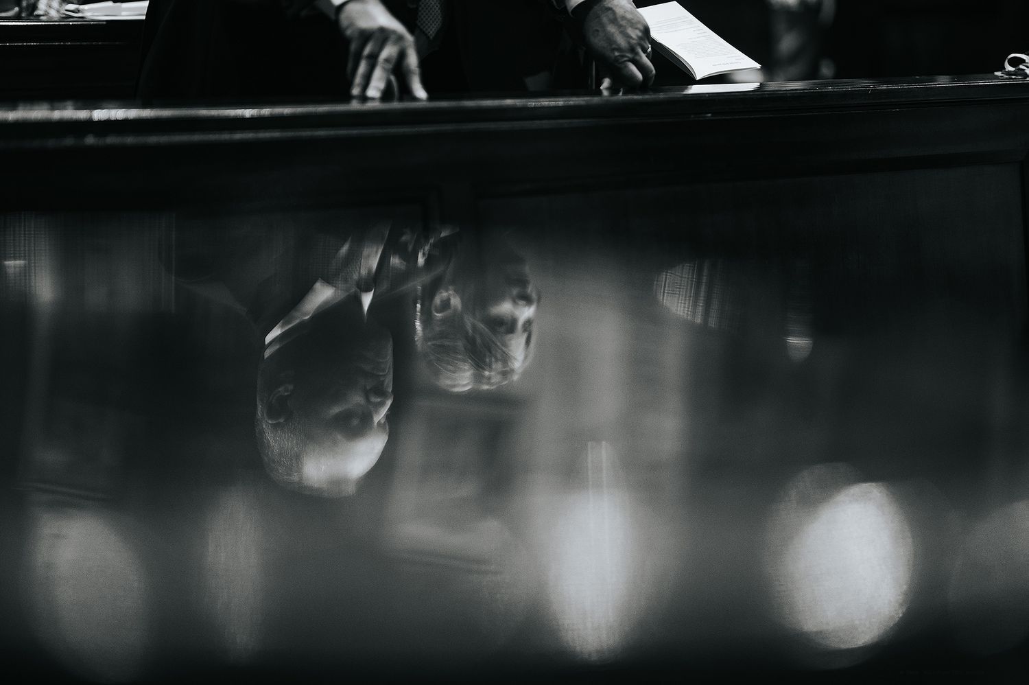 Black and white artistic photo of wedding rings reflected in polished surface with blurred bokeh background.
