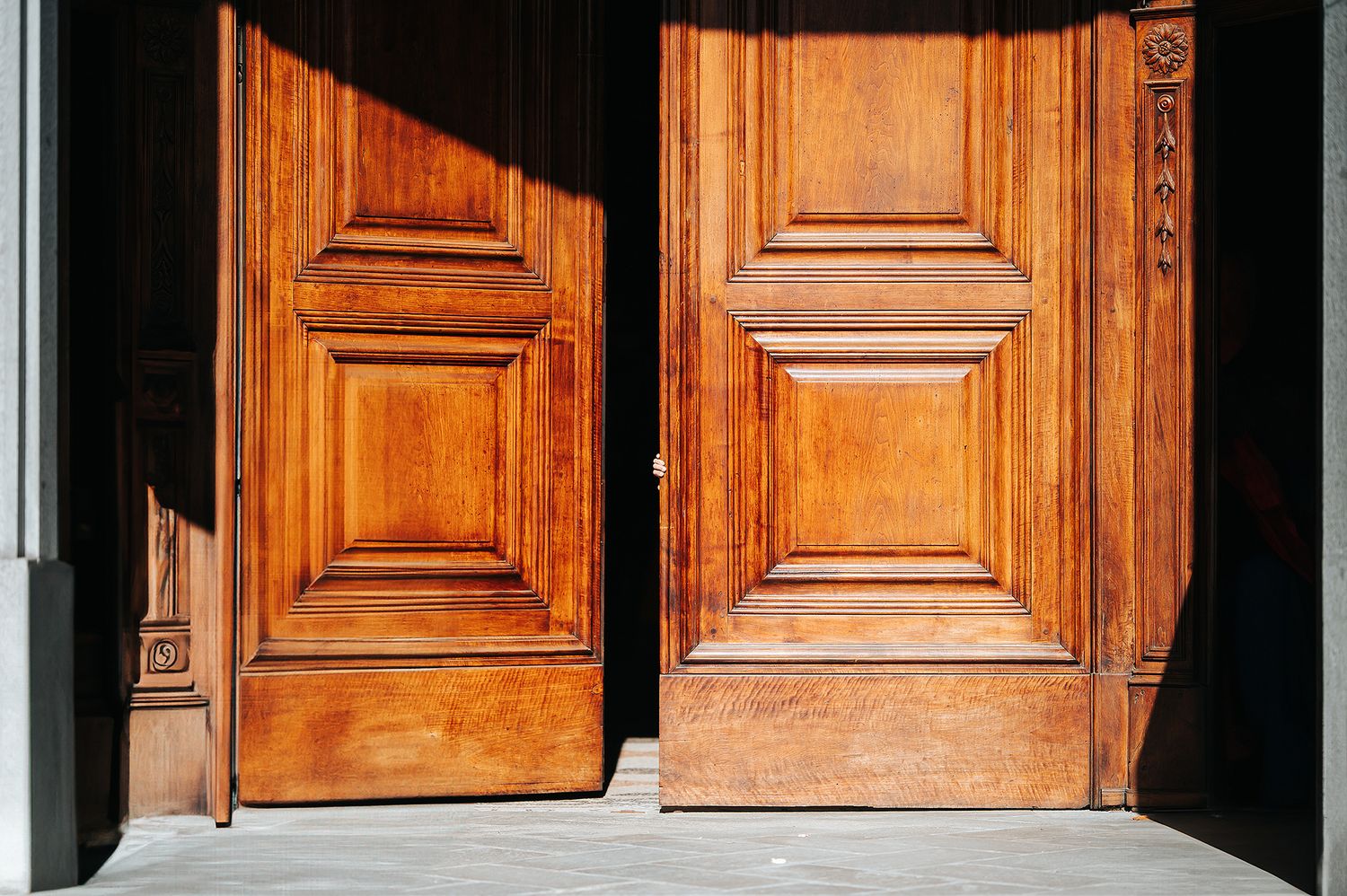 Classic ornate wooden double doors of a church entrance bathed in warm sunlight.