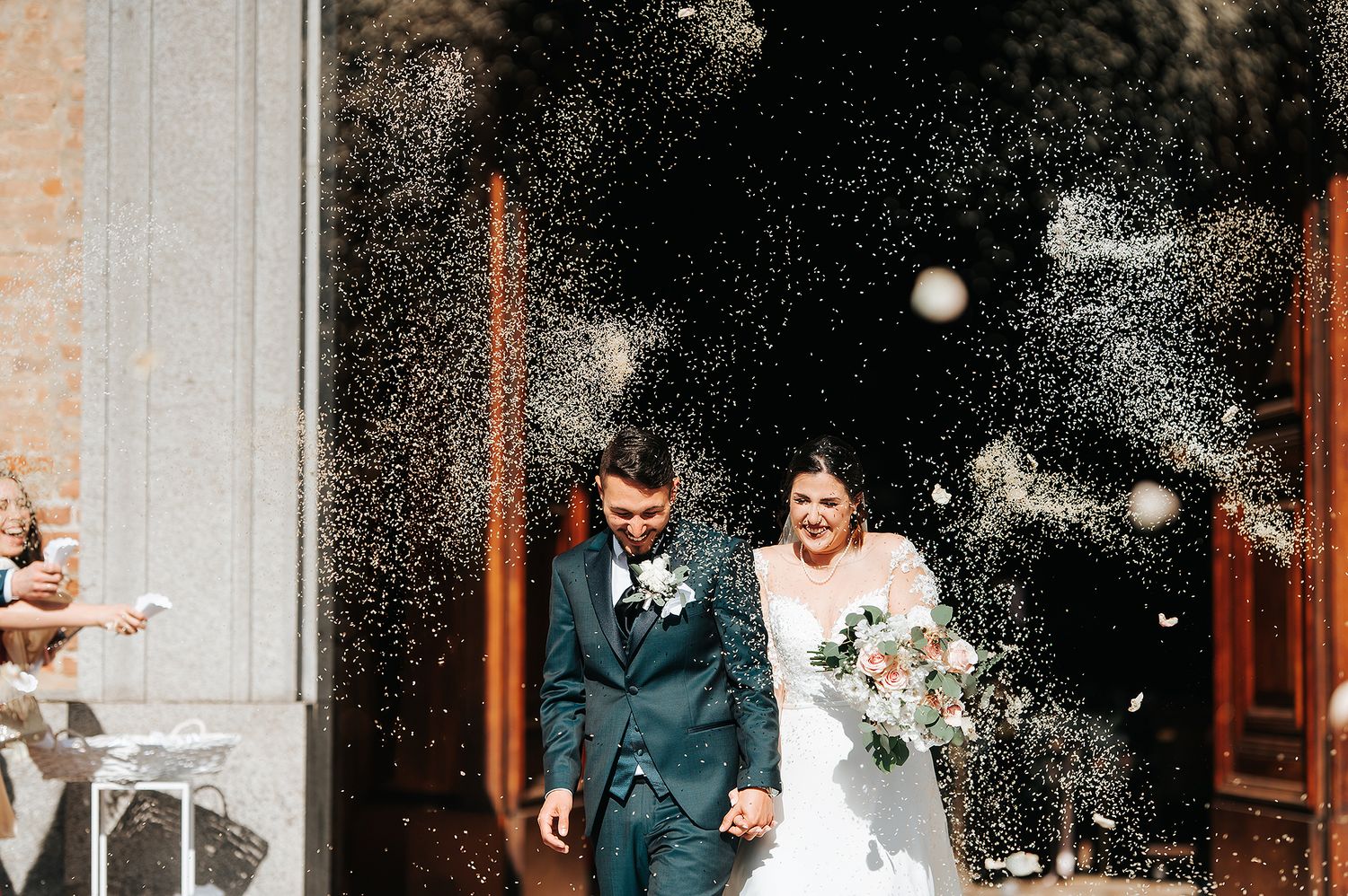 Bride and groom exiting church through shower of rice thrown by celebrating wedding guests.