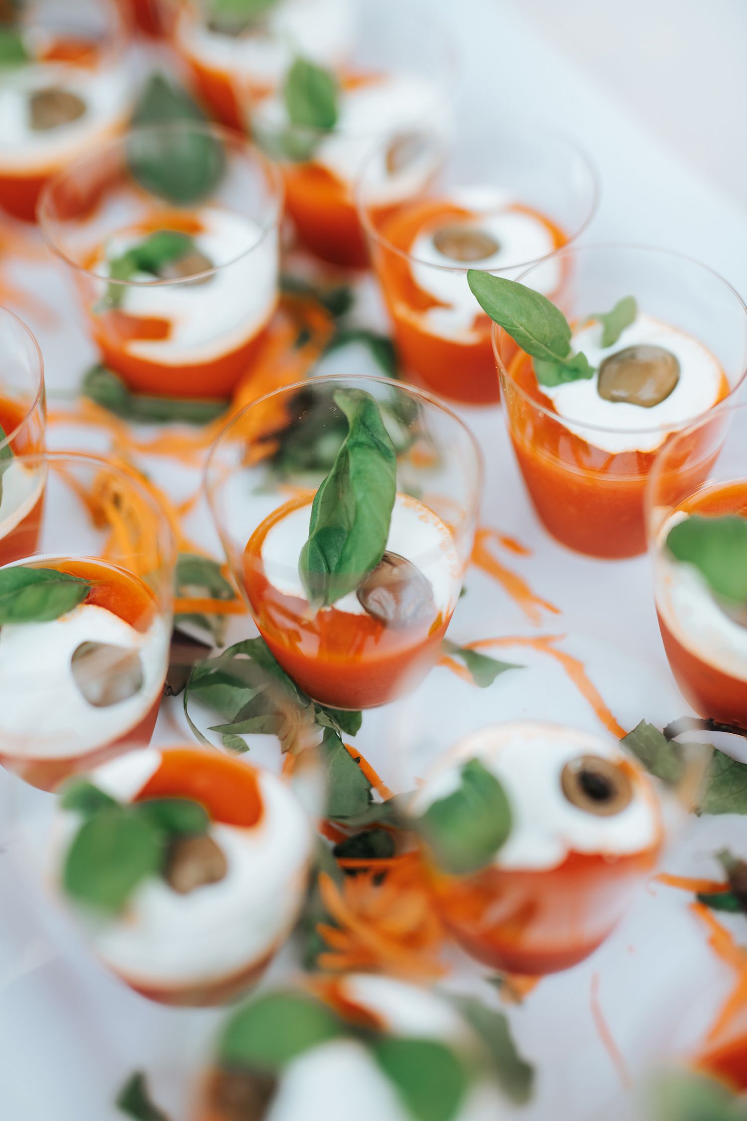 Elegant appetizers of tomato gazpacho with cream and basil in small glasses on a tray.