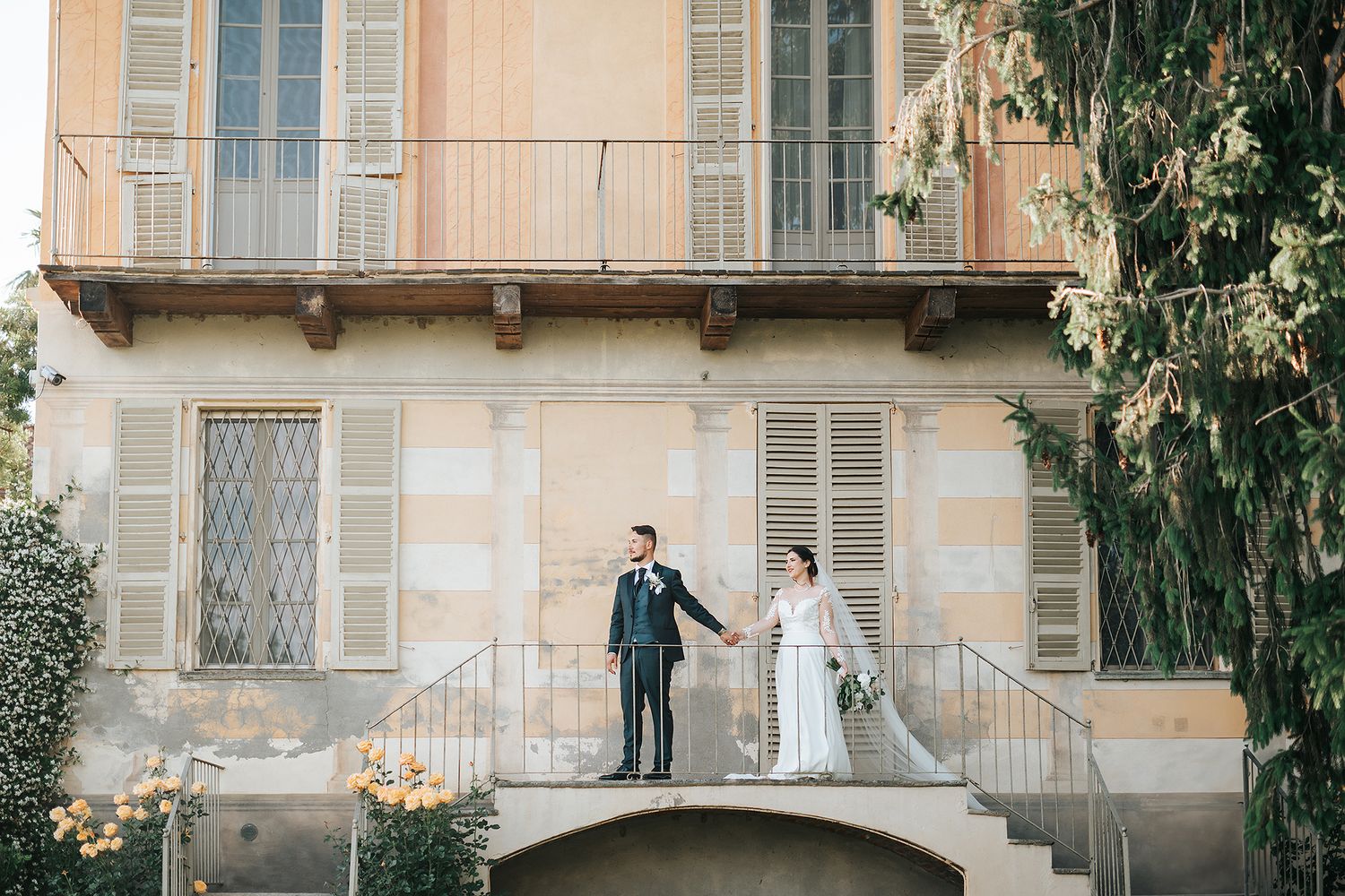 Bride and groom hold hands on a stone terrace of a classic Italian villa.