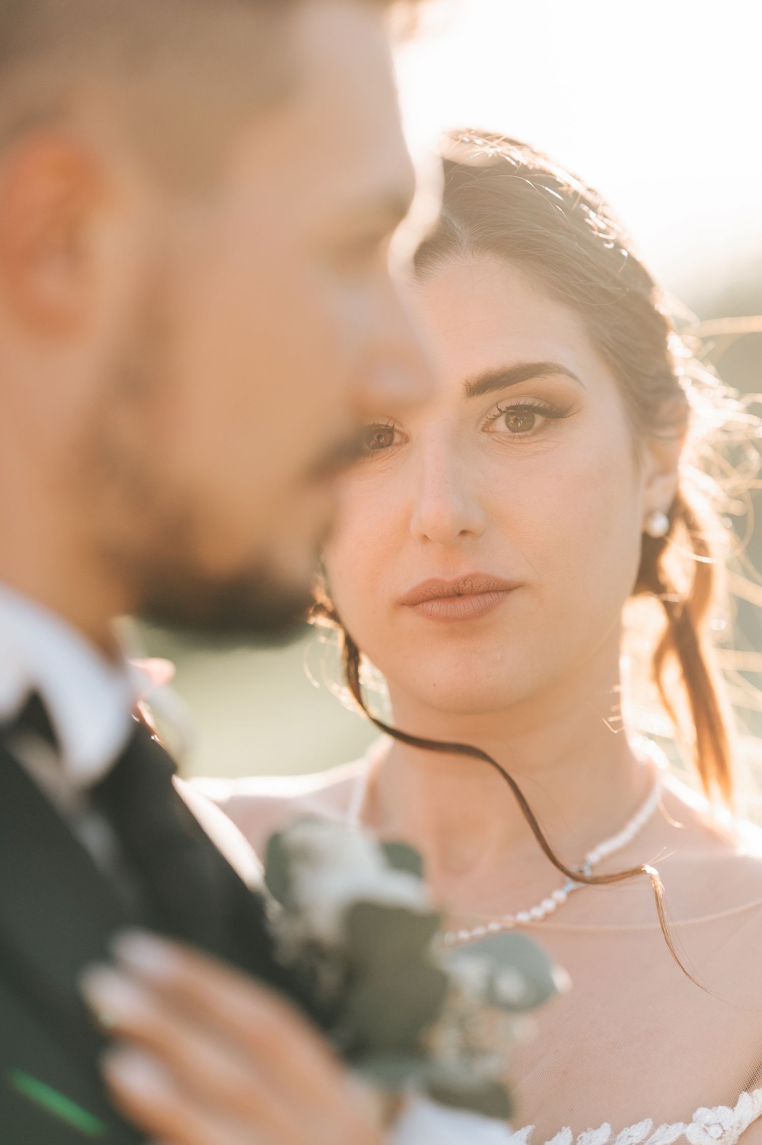 Close-up portrait of a bride with pearl necklace gazing softly beside her groom.