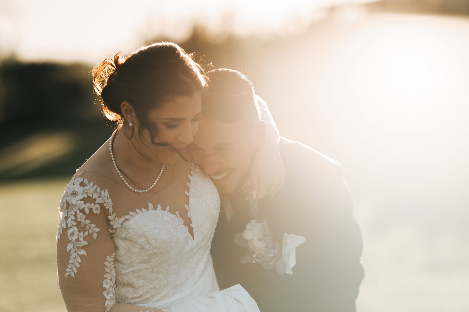 Bride and groom laugh joyfully together in warm golden sunset light outdoors.