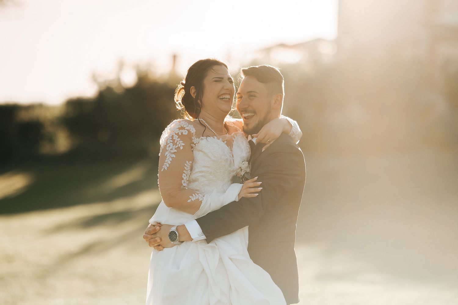 Happy bride and groom embracing outdoors in warm golden sunlight on their wedding day.