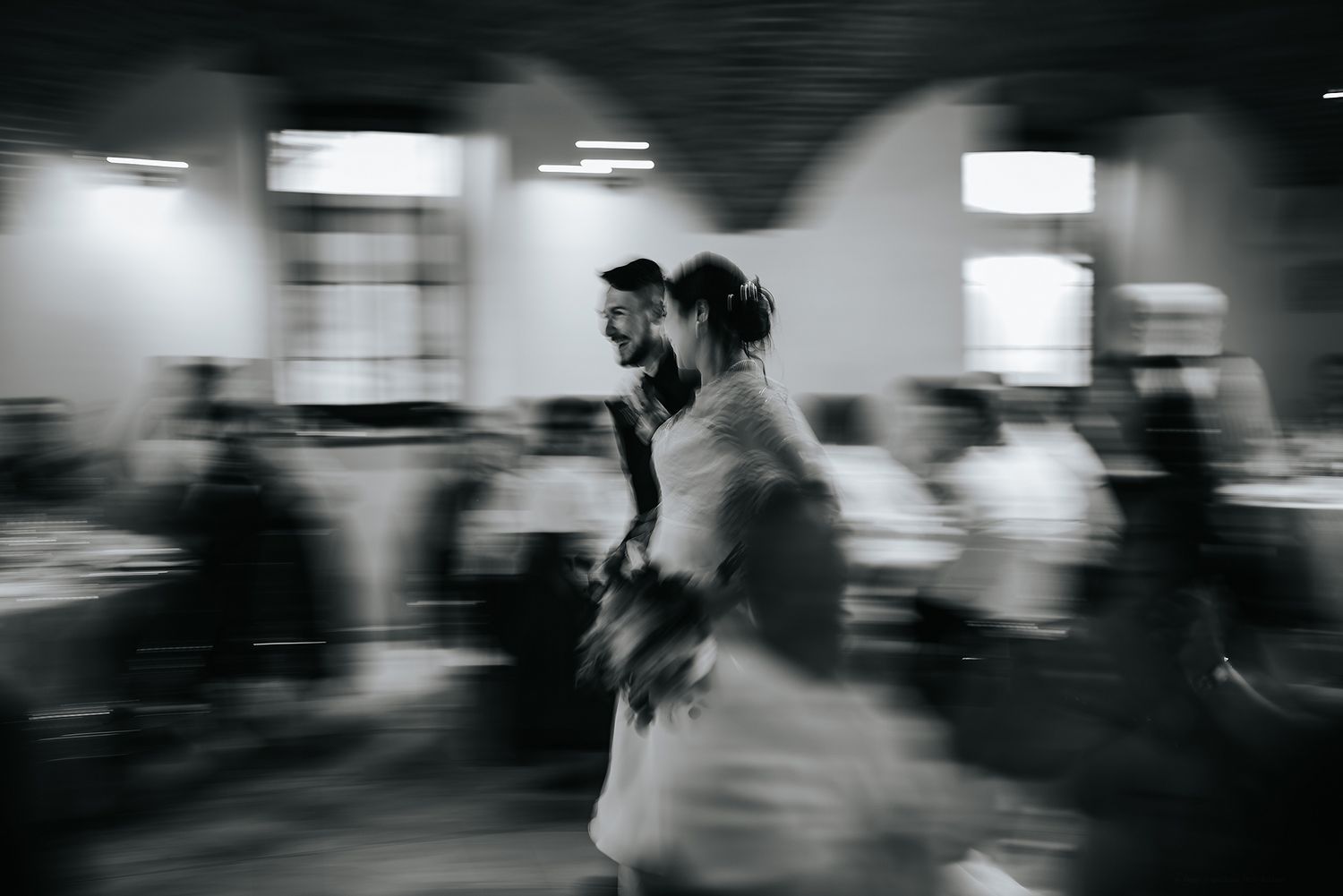 Artistic blurred black and white photo of bride and groom moving through wedding reception.