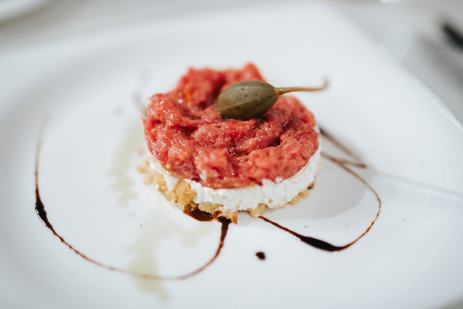 Elegant tomato tartare with cream cheese and caper on white plate with balsamic drizzle.
