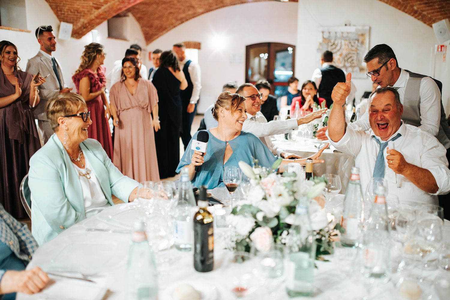 Lively wedding reception guests laughing and celebrating together at elegantly decorated dinner tables.