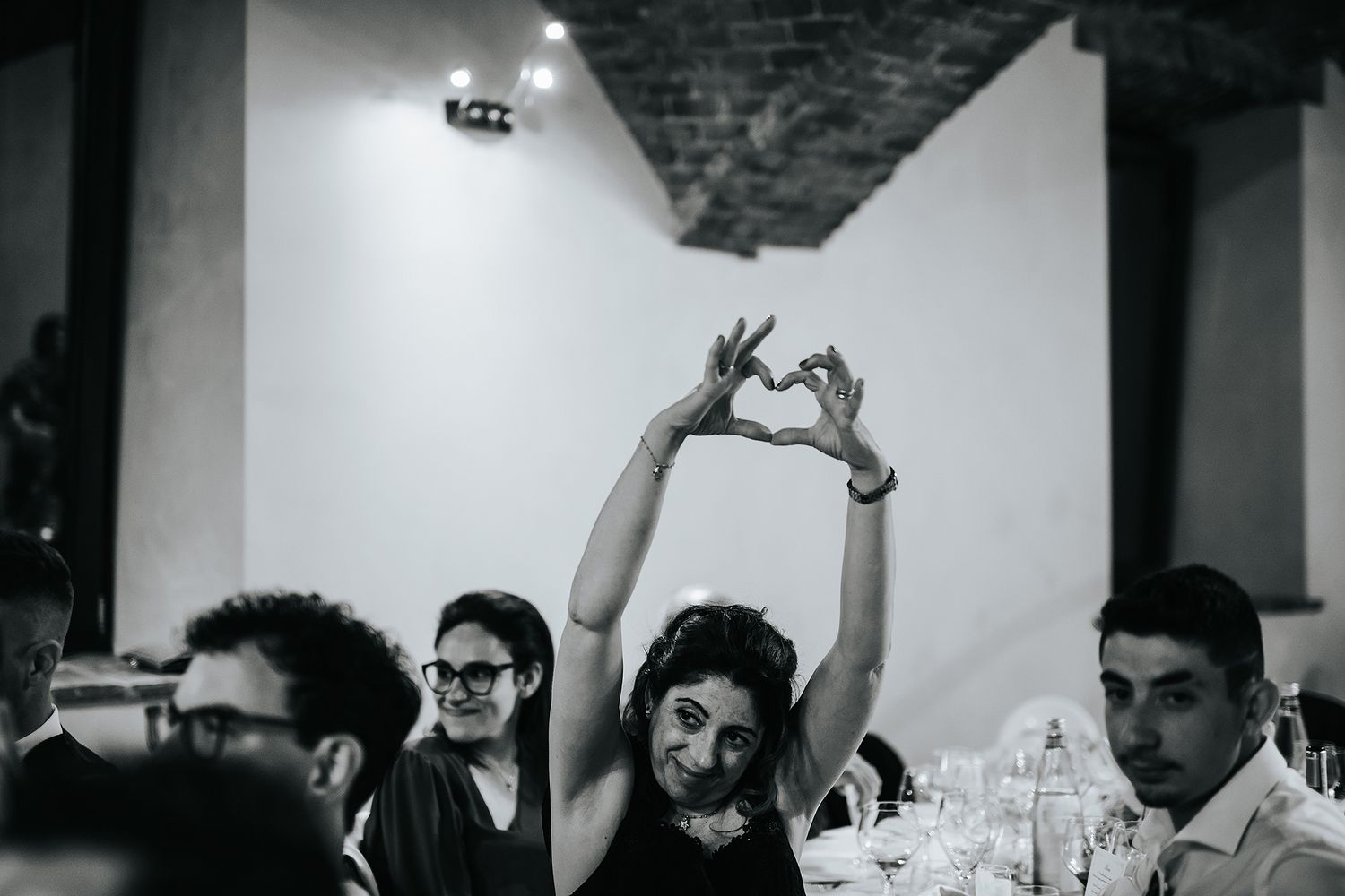 Wedding guest making heart shape with hands above head during fun reception celebration.