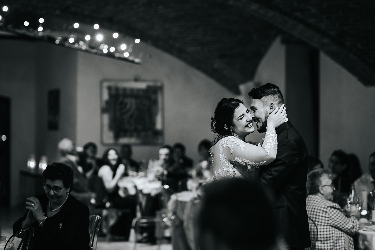 Newlyweds share romantic first dance while wedding guests watch in elegant vaulted venue.