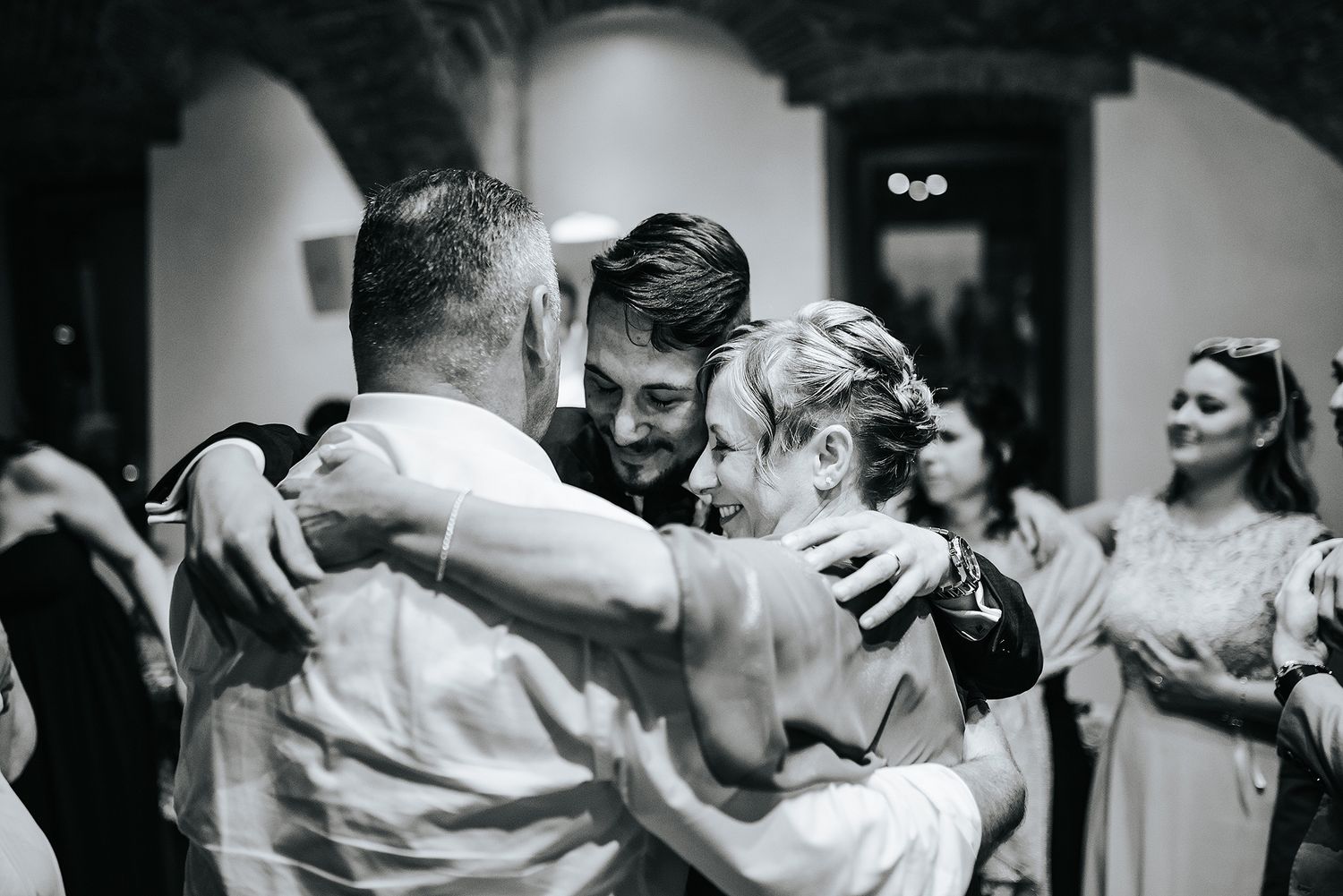 Emotional group hug between wedding couple and guest captured in black and white photo.