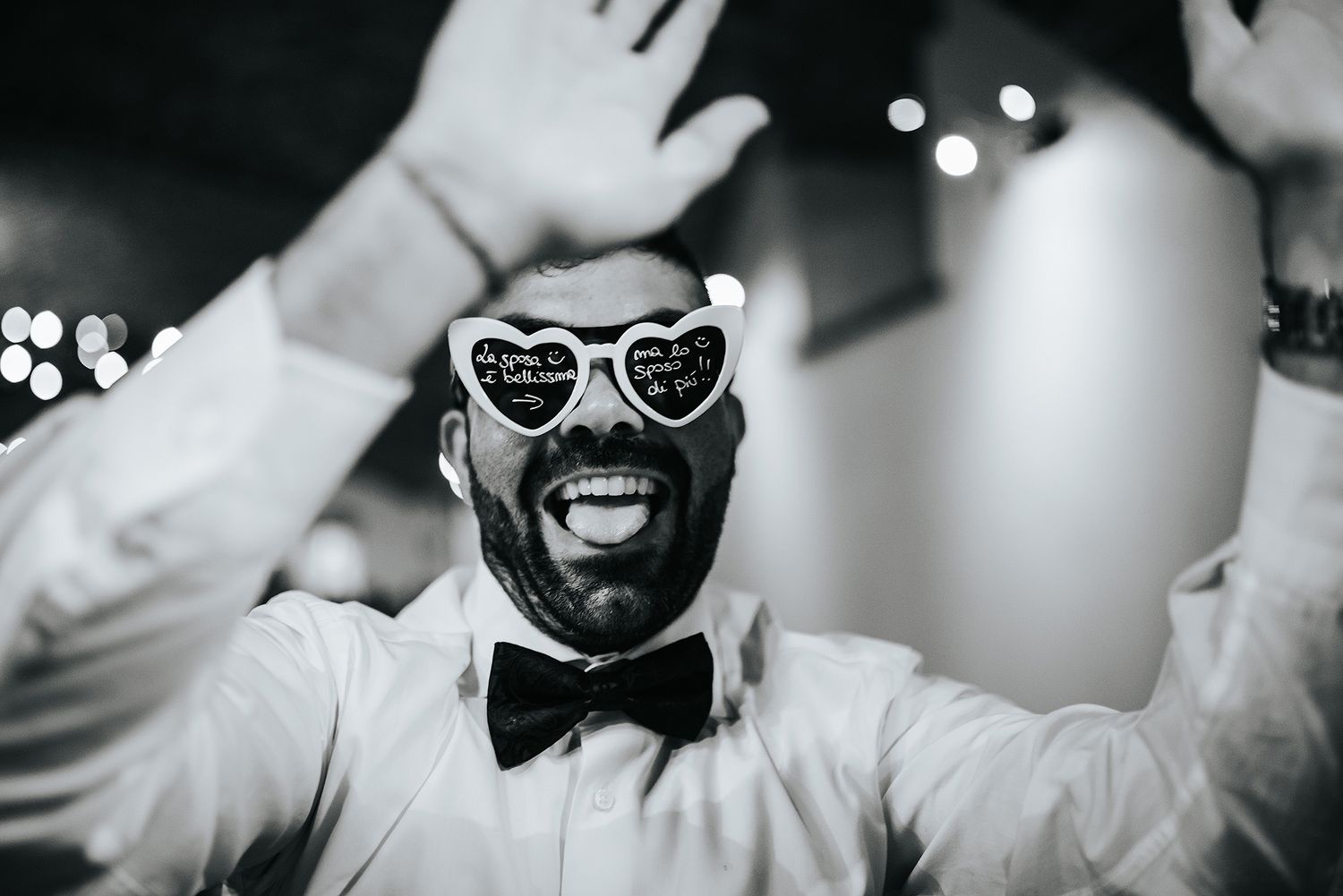Excited wedding guest wearing heart-shaped novelty sunglasses celebrating at reception party.