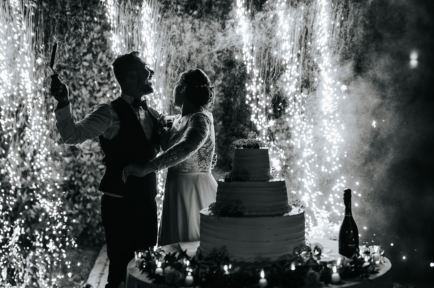 Bride and groom cutting wedding cake with sparkler fountains in black and white photography.