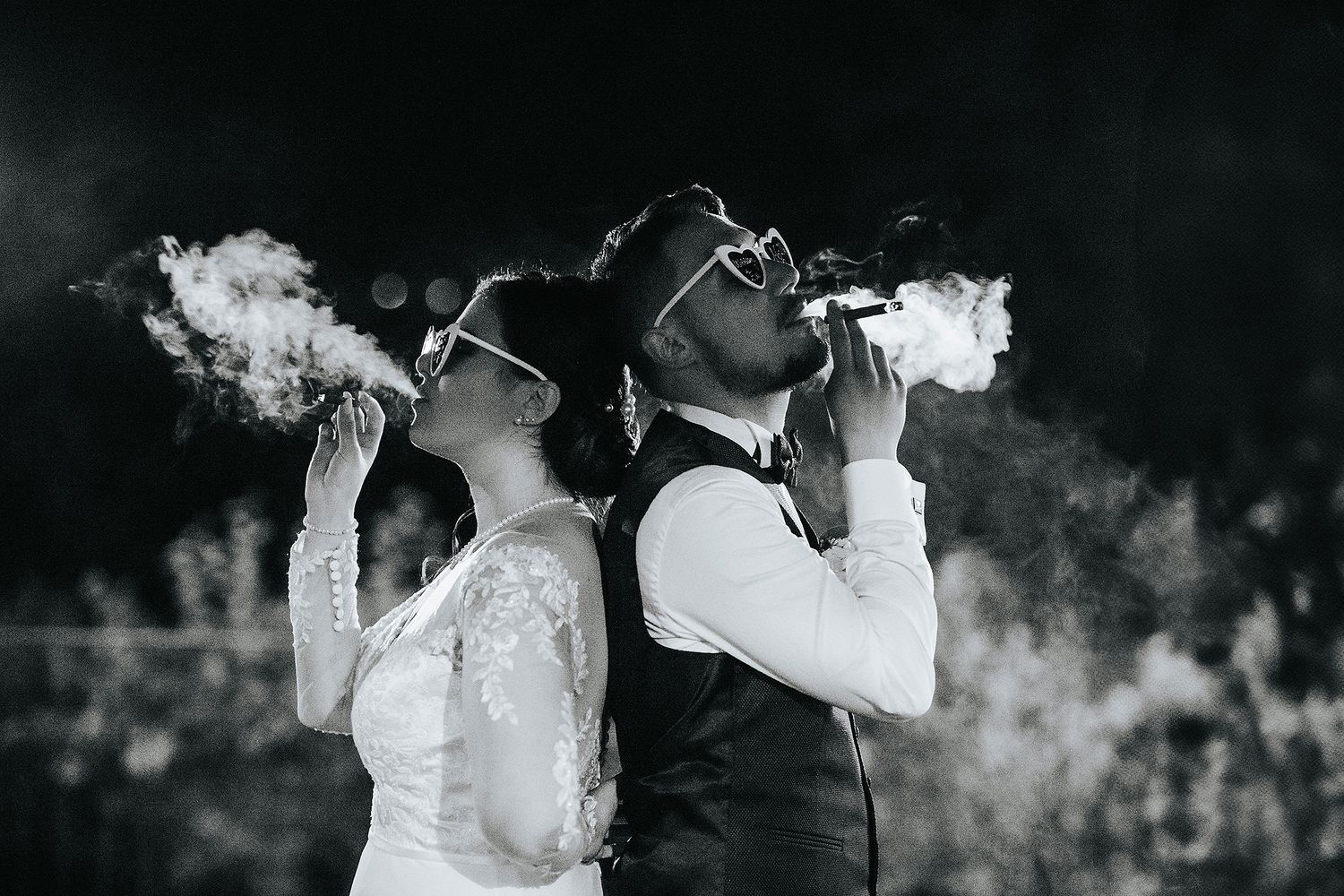 Bride and groom smoking cigars back to back in stylish black and white wedding portrait.