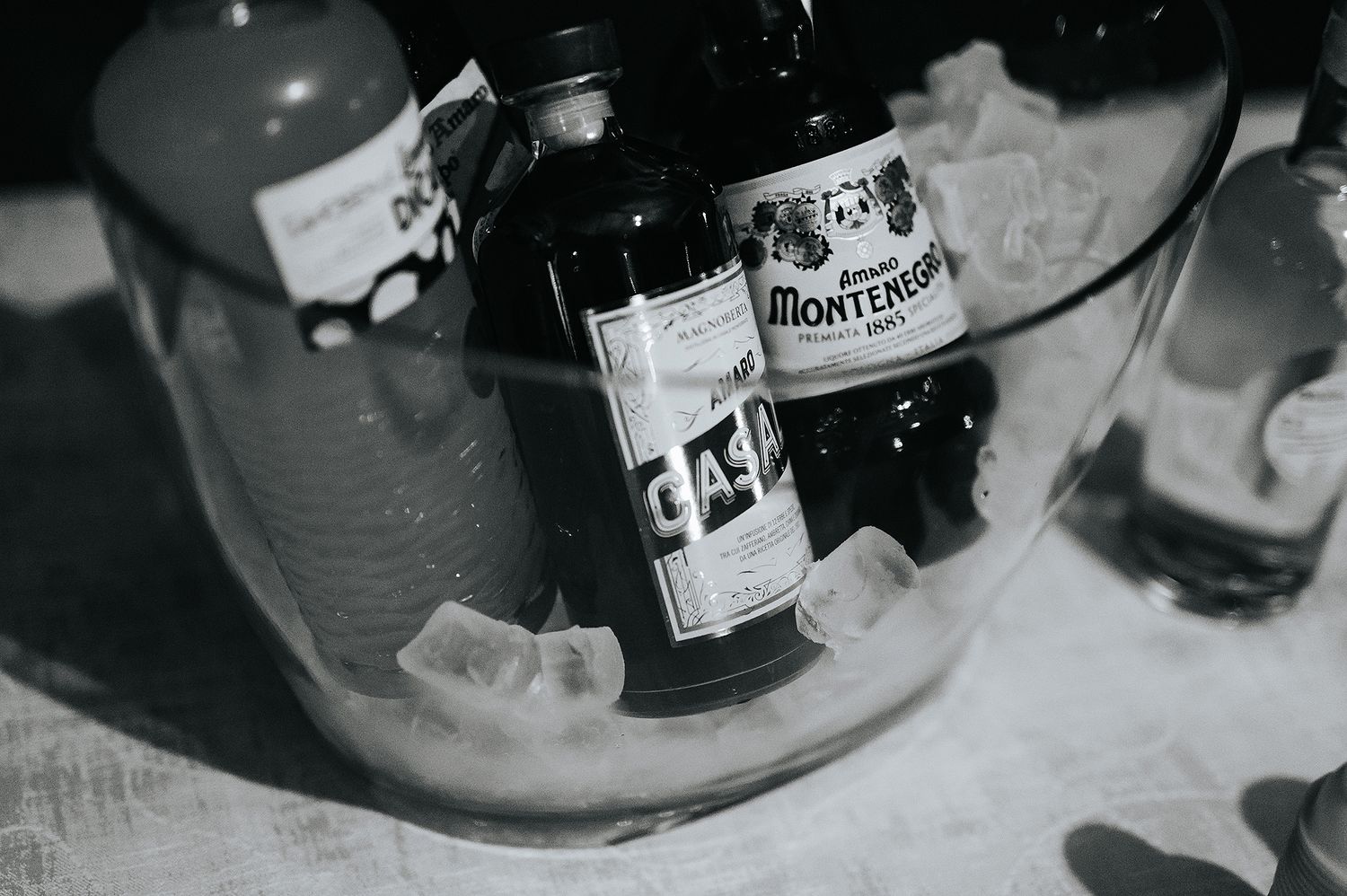 Black and white close-up of Montenegro liqueur bottles chilling in ice bucket at wedding reception.